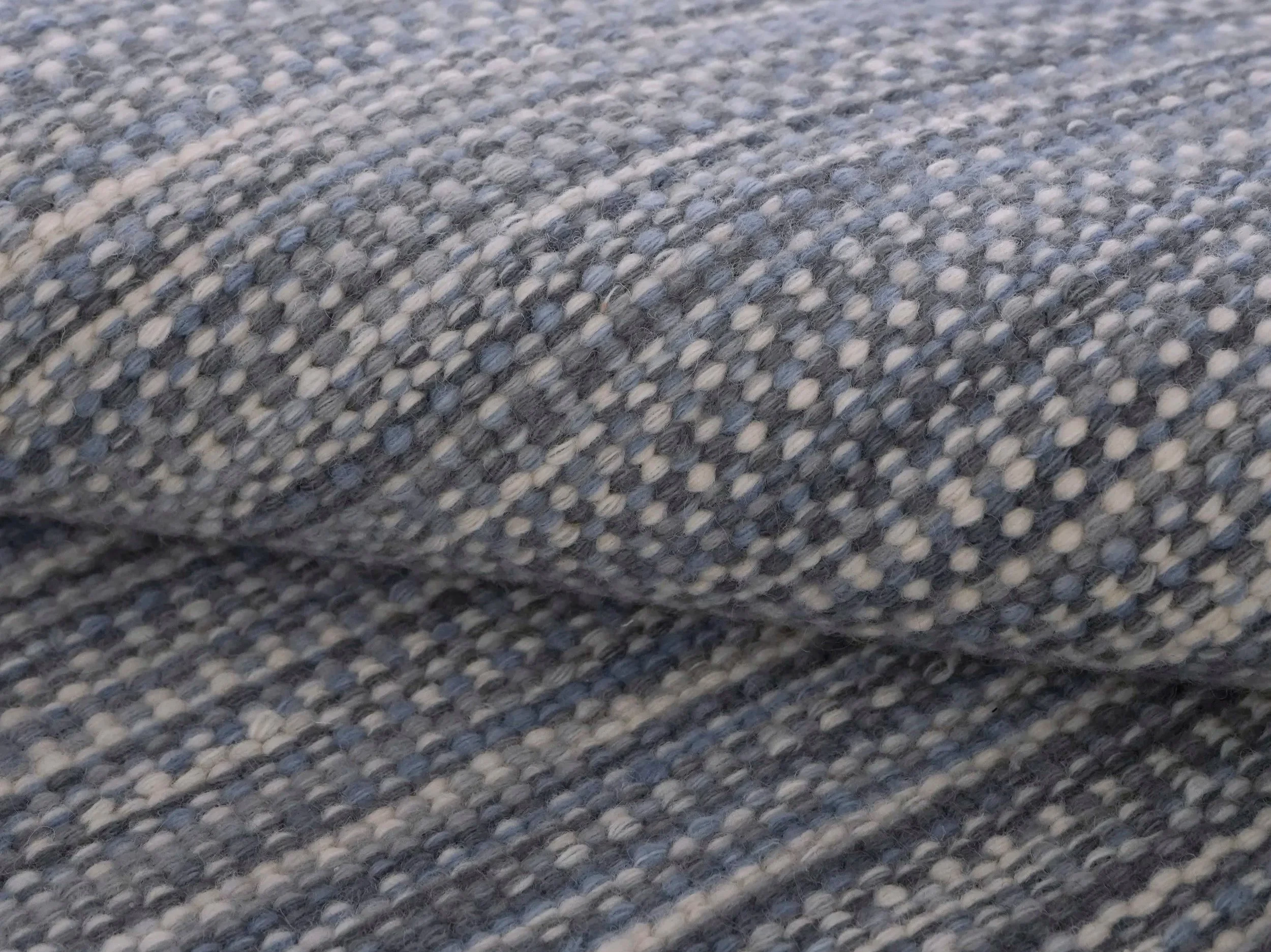 Close-up of a textured woven fabric in shades of gray, white, and black with a patterned, striped design.