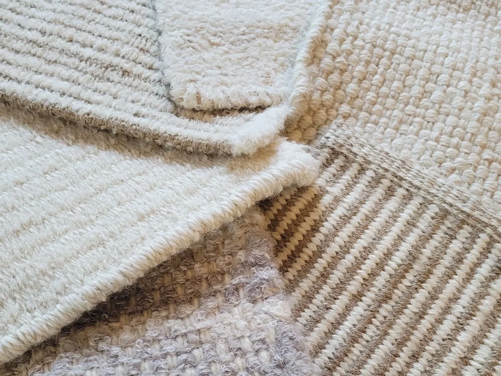 Close-up of three stacked woven rugs or towels in beige, tan, and cream colors with different textured patterns.