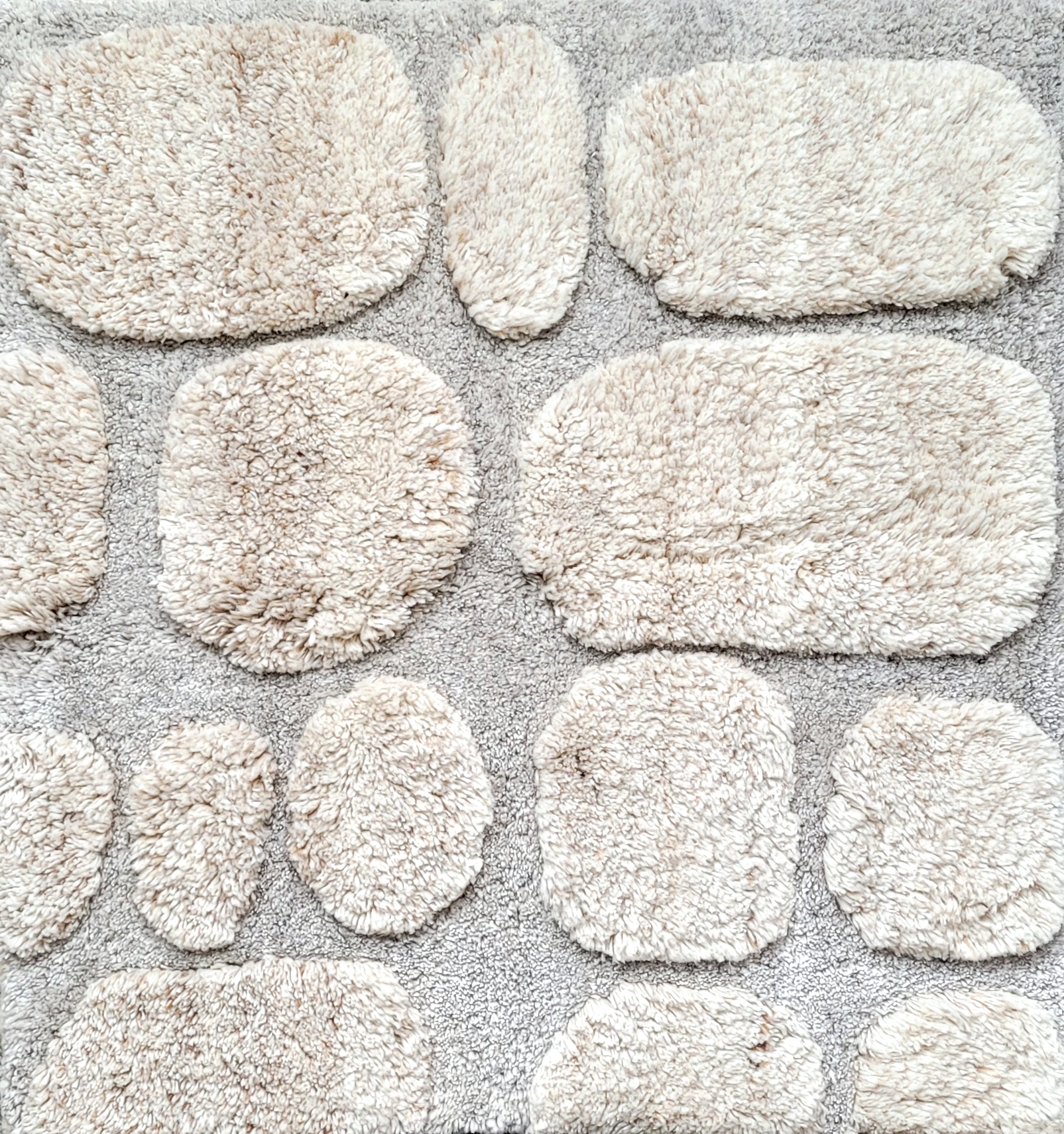 A collection of fluffy, beige bath rugs with oval and circular shapes on a carpeted floor.