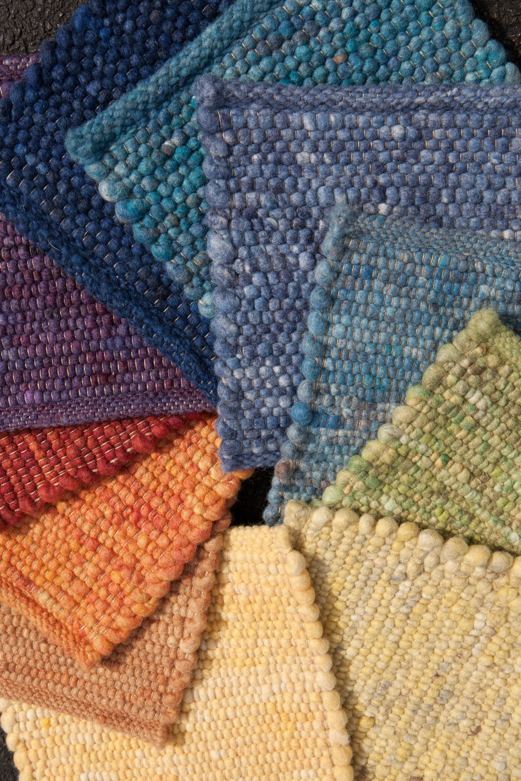Close-up of a variety of colorful woven textile pieces in shades of blue, purple, red, orange, yellow, and cream.