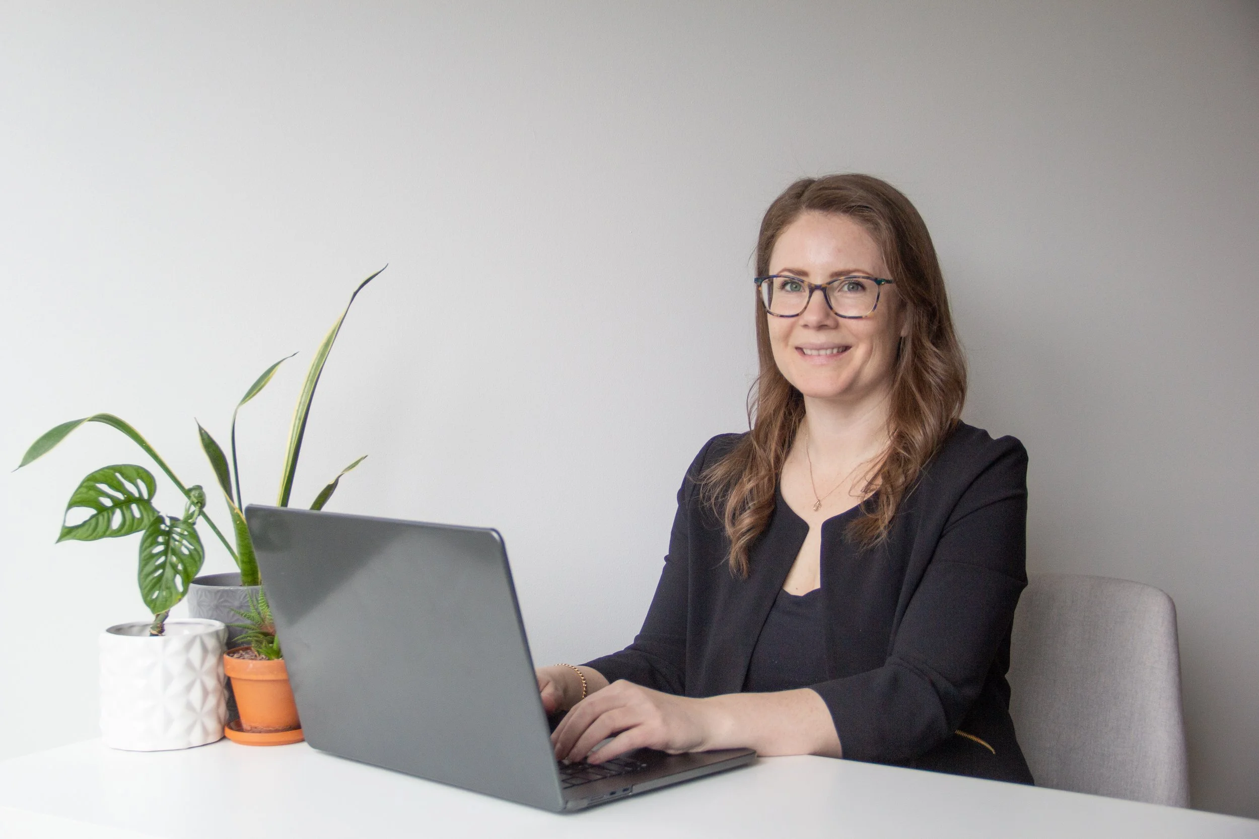 A person writing in a notebook with a pen, wearing a white long-sleeve shirt, a pink bracelet, and a black watch, sitting at a table with a glass of water nearby.