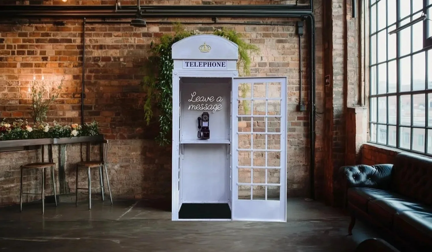 A vintage white telephone booth with a sign that says "Leave a message" and a rotary telephone inside.