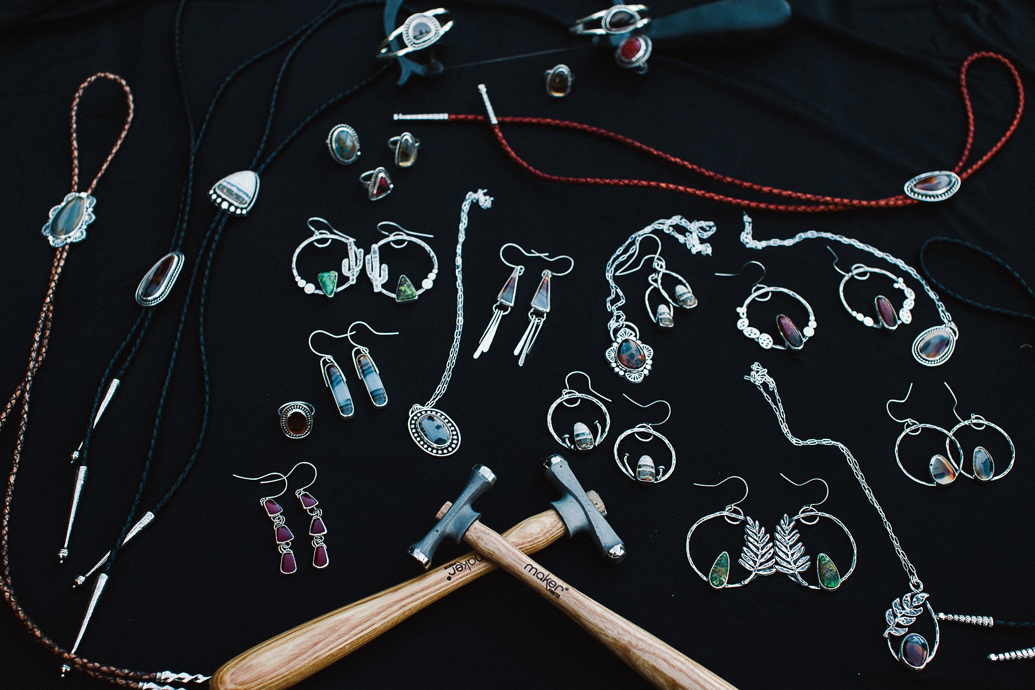 Jewelry display on black fabric including necklaces, earrings, and rings along with two hammers.