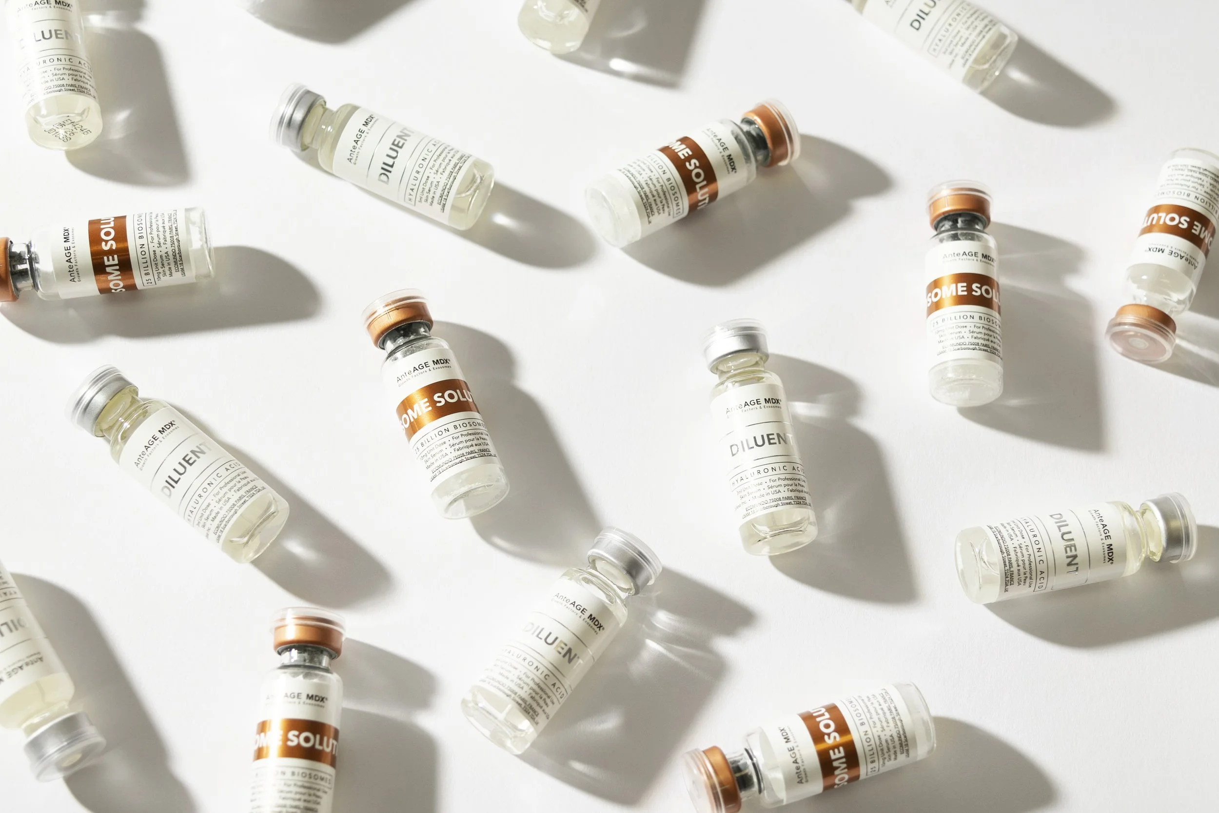 Several small glass vials with white and orange labels scattered on a white surface, casting shadows.
