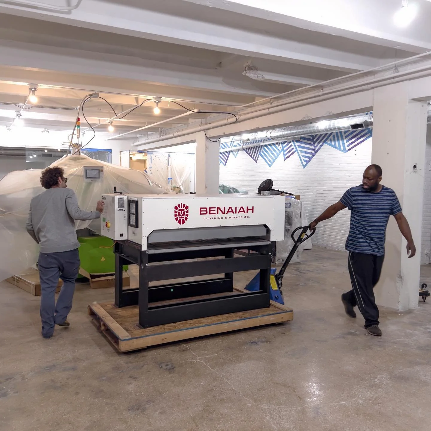 Ashley and man moving cure dryer into new print shop on a pallet jack