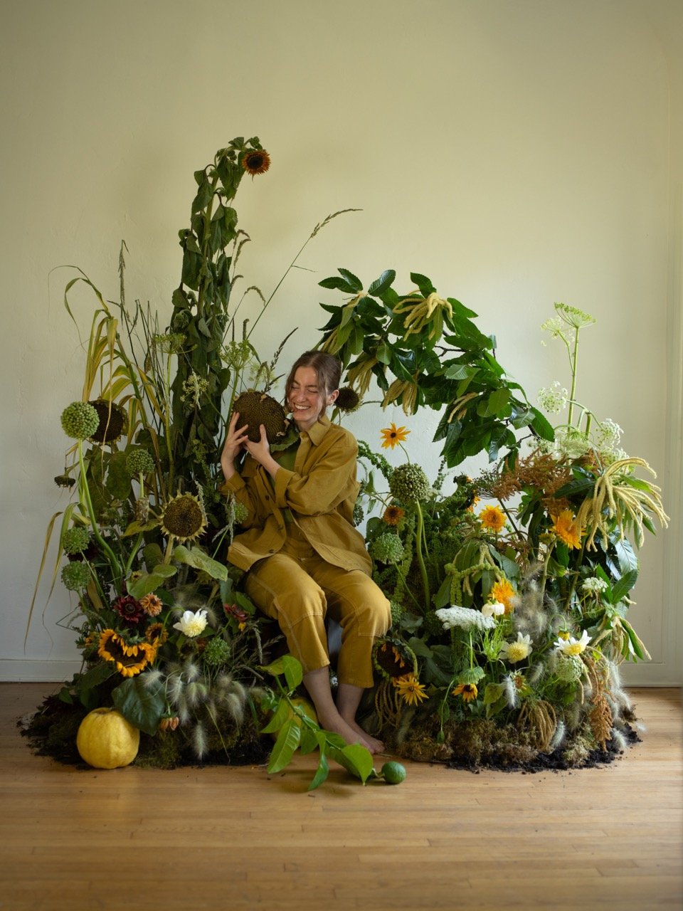 A woman in yellow workwear sitting in a lush setting