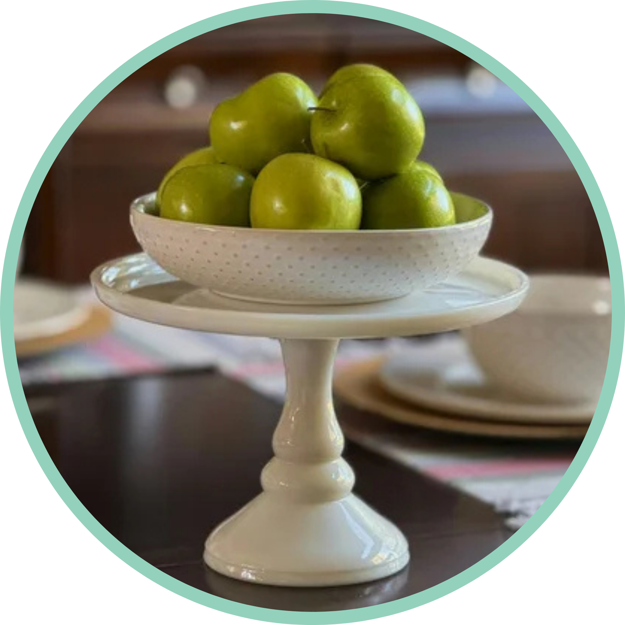 Meal Planning. A white ceramic tiered serving stand holding green apples on top and a piece of fruit in the lower left corner.