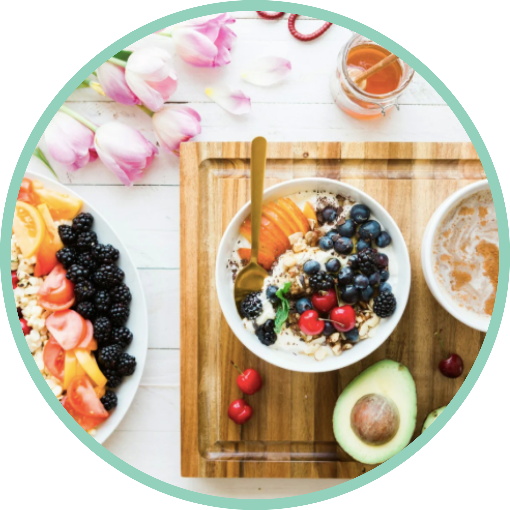Assorted bowls of yogurt topped with fresh fruit and granola, on a wooden tray, surrounded by pink tulips and honey jar with a dipper, on a white wooden surface.