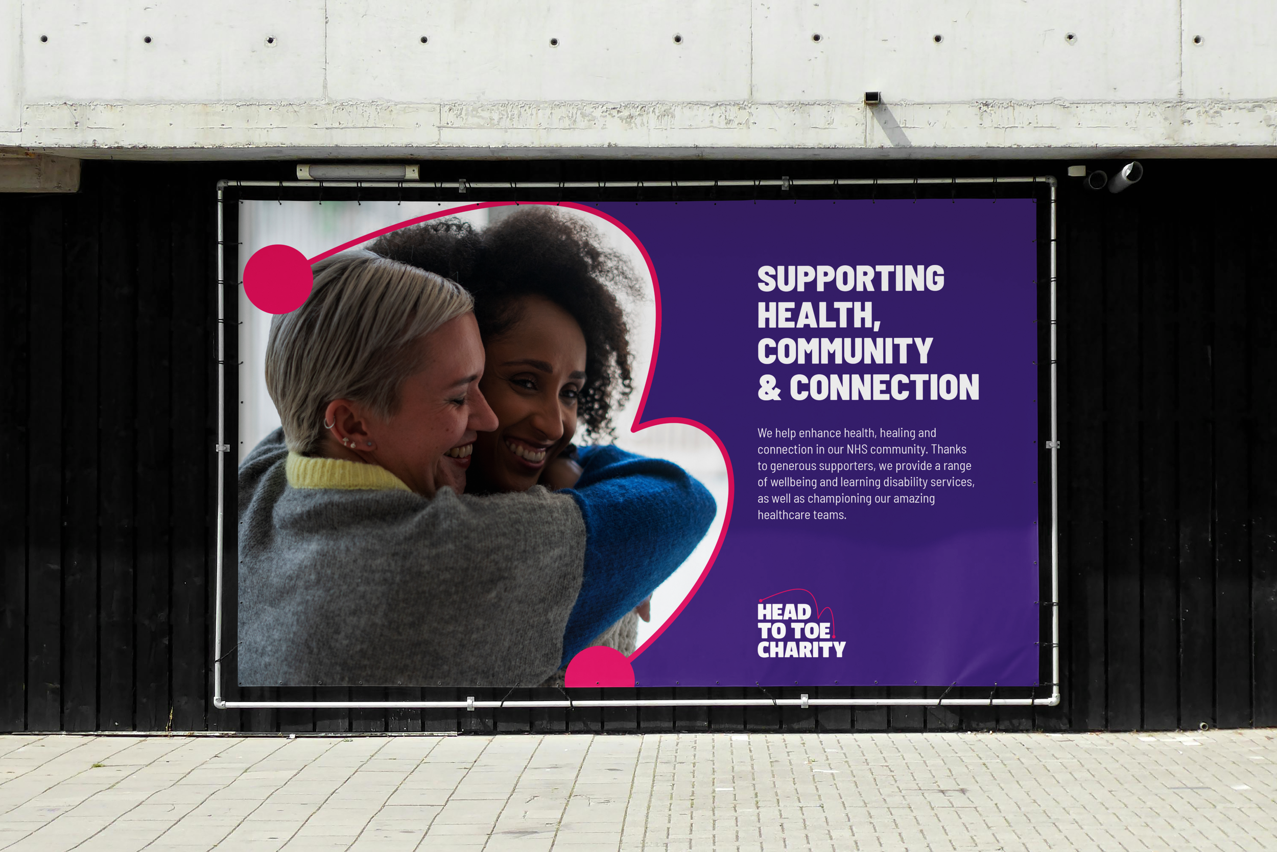A billboard for Head to Toe Charity featuring the new brand. The billboard has an image of two hugging, smiling women, and the text 'Supporting Health, Community and Connection'.