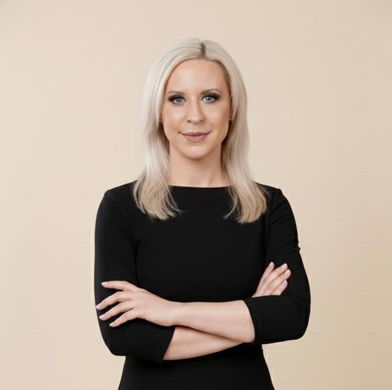 A woman with platinum blonde hair, wearing a black top, standing in front of white cabinets.