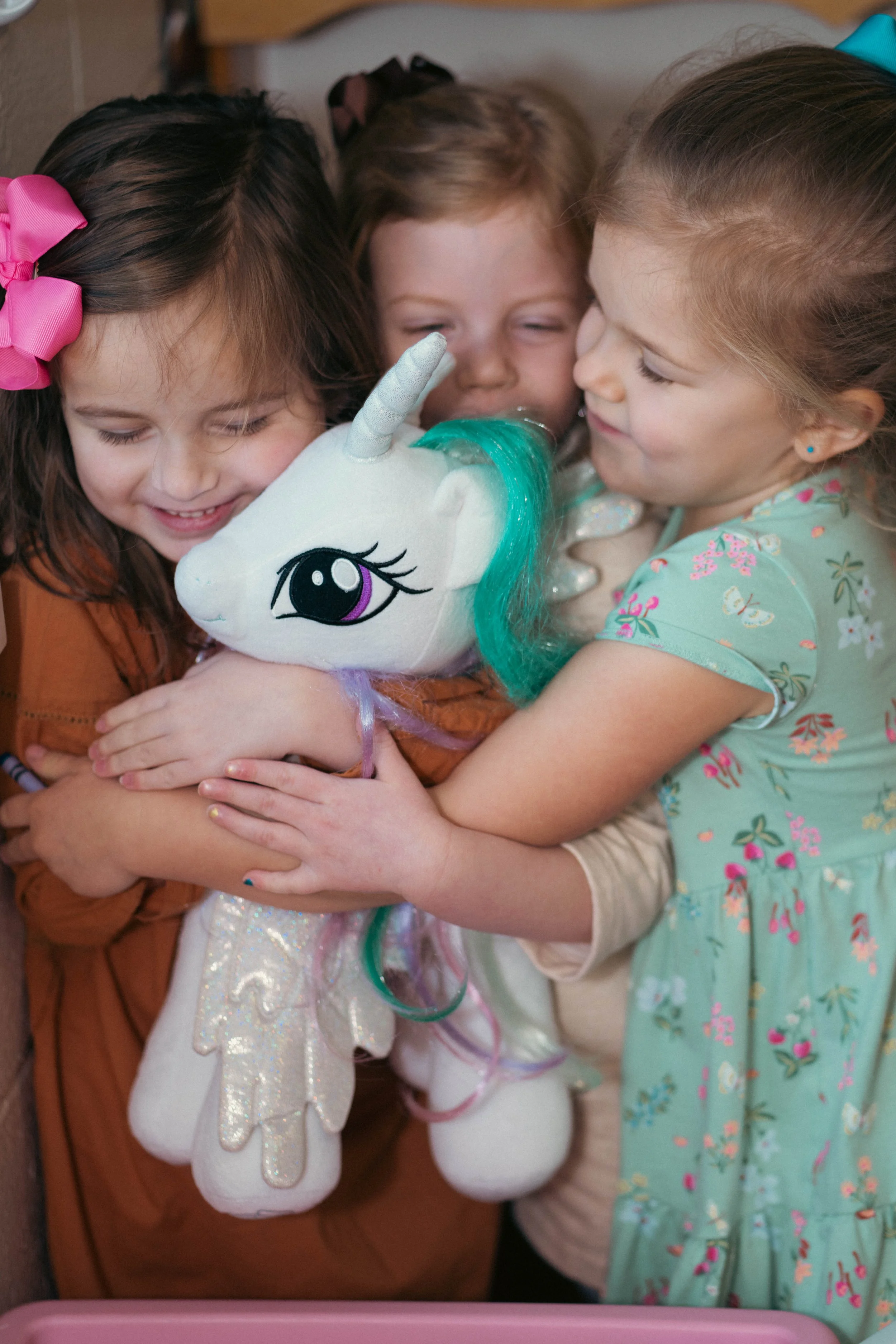 Three young girls hugging a plush toy unicorn.