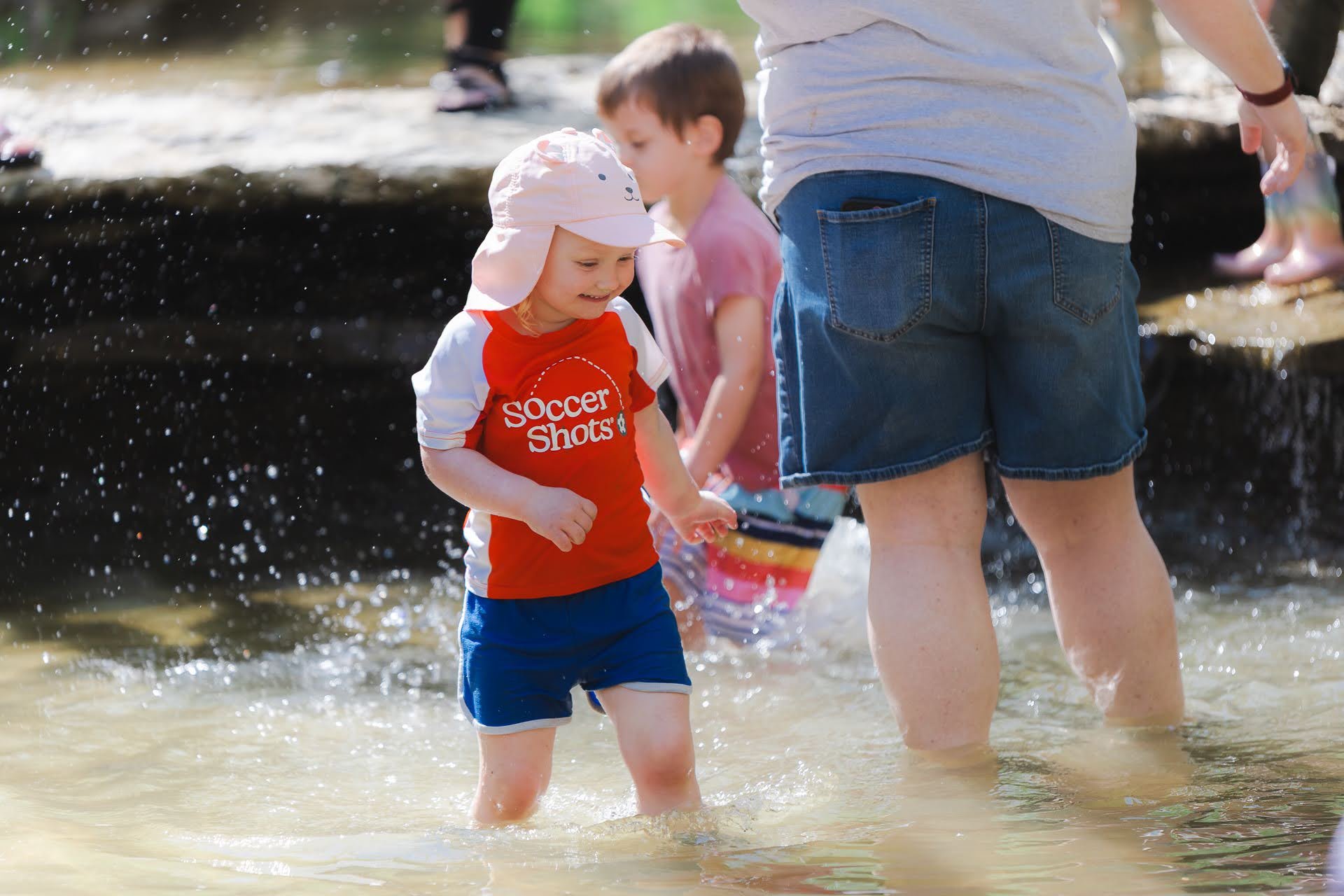 Children playing in a shallow creek on a sunny day, with an adult supervising.
