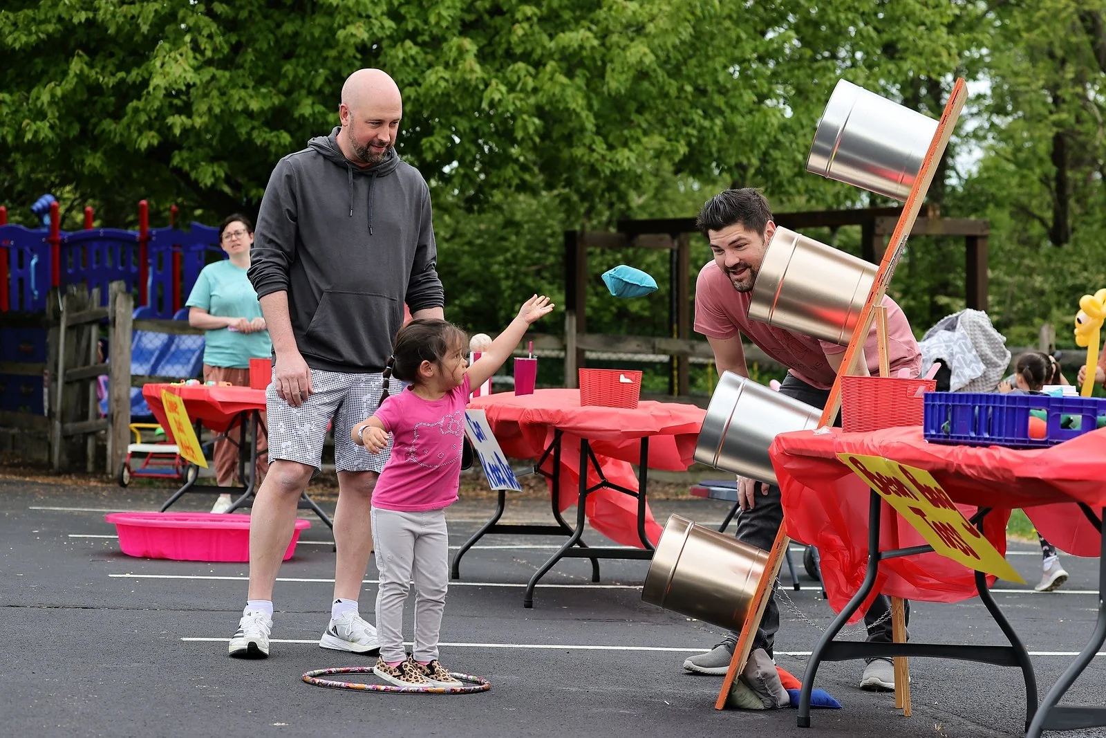 A young girl at a carnival dunk tank game hitting a target to dunk a man into the water, with a man and woman observing nearby.