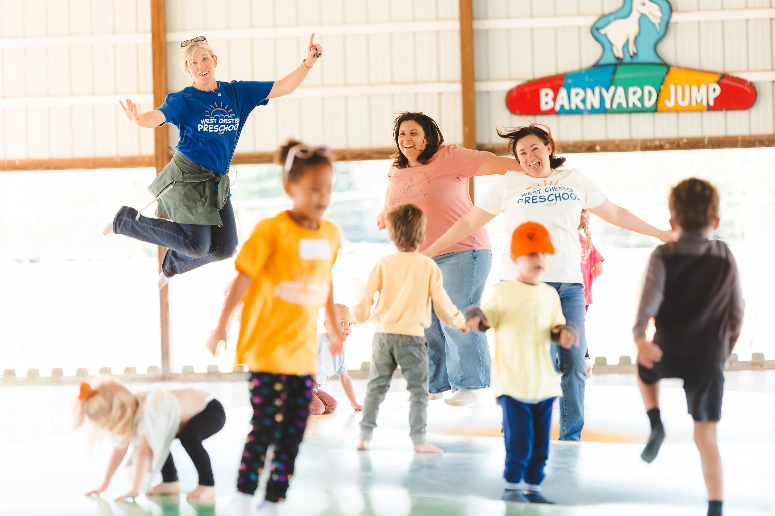 Children and adults playing and jumping inside a barnyard jump area at a preschool.