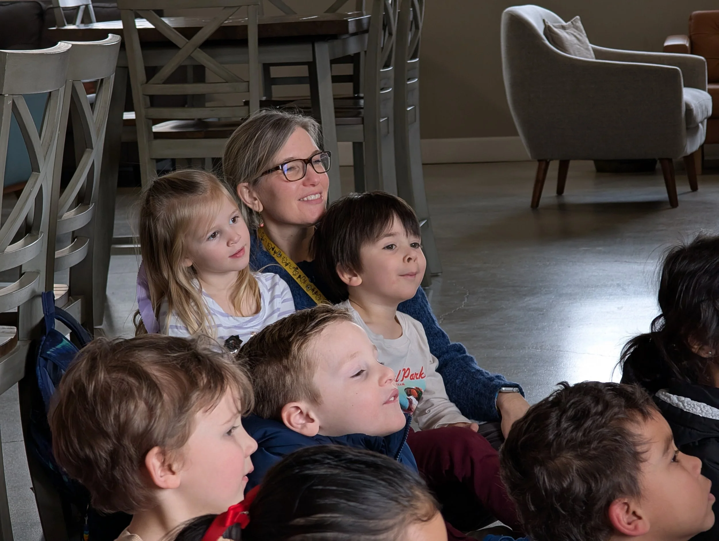 Group of children and a woman sitting on the floor, watching something attentively.