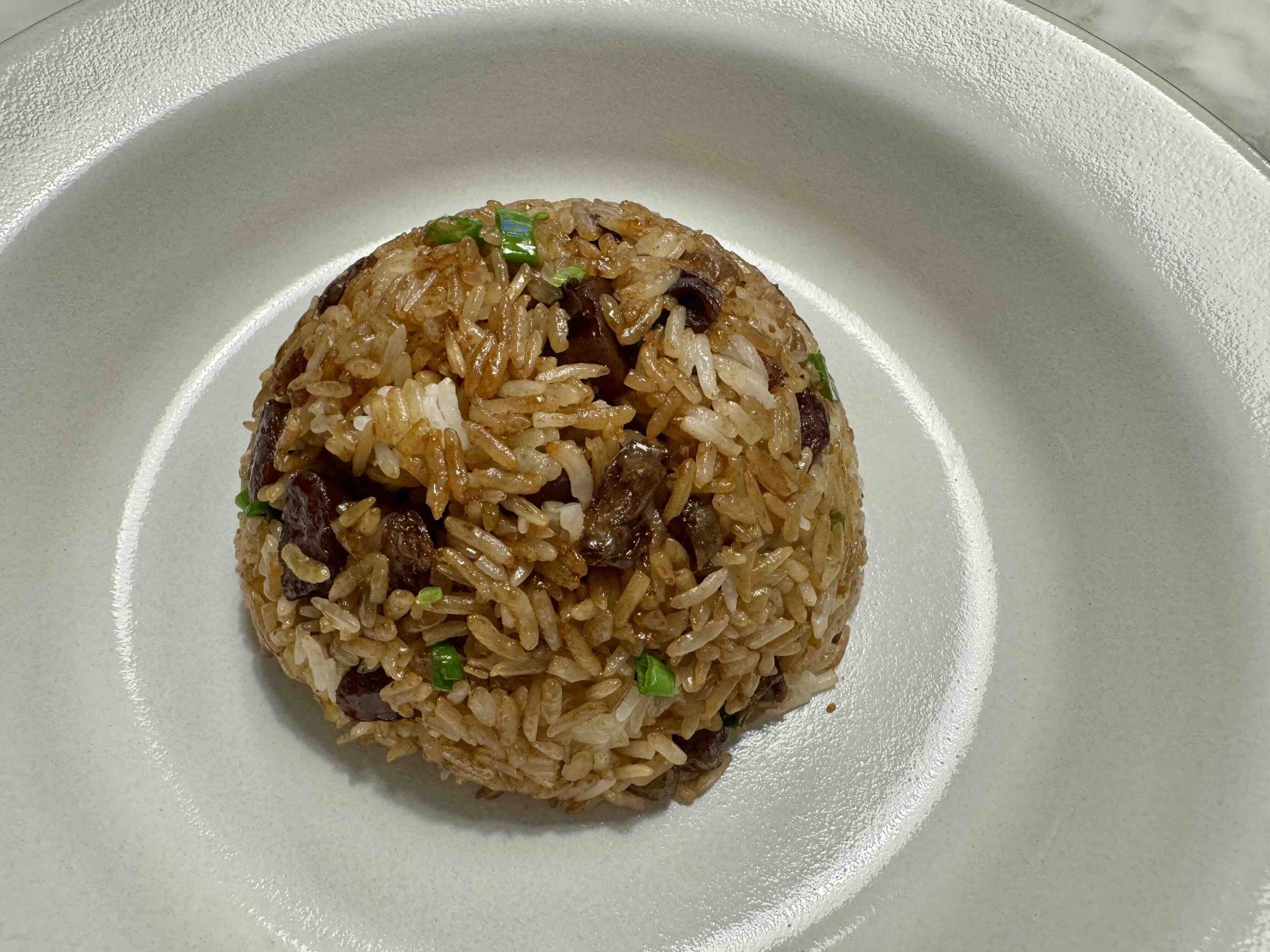 Cantonese sticky rice with Chinese sausage, cured pork belly, and scallions molded into a bowl shape on a pale plate