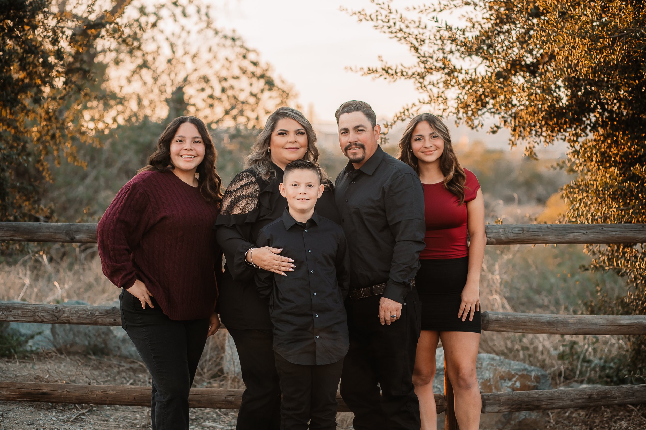 Family of five in burgundy and black at a wooden fence in golden hour light at Iron Horse Trailhead, Santa Clarita.