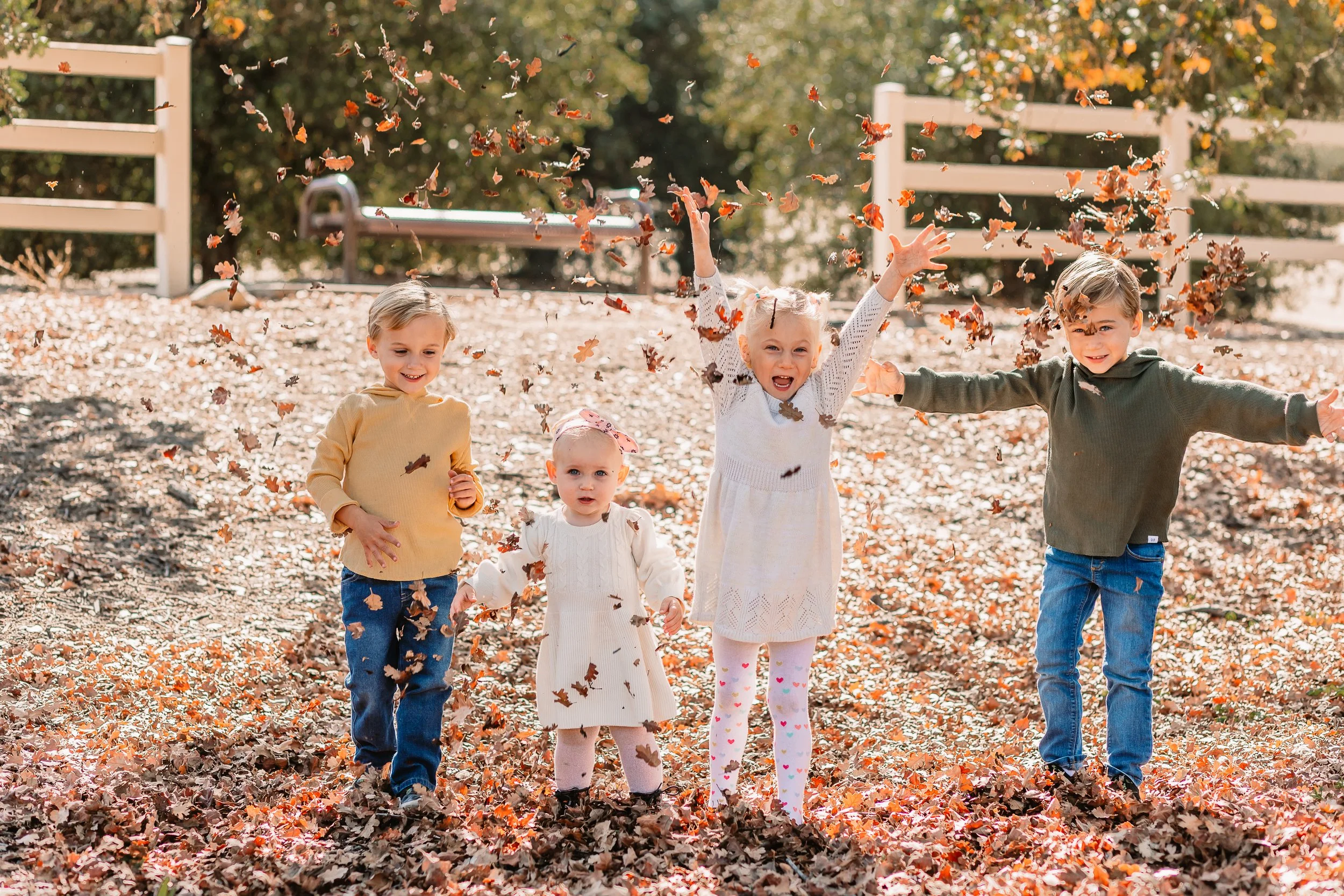 Four kids laughing and throwing autumn leaves during a fall mini session in Santa Clarita.