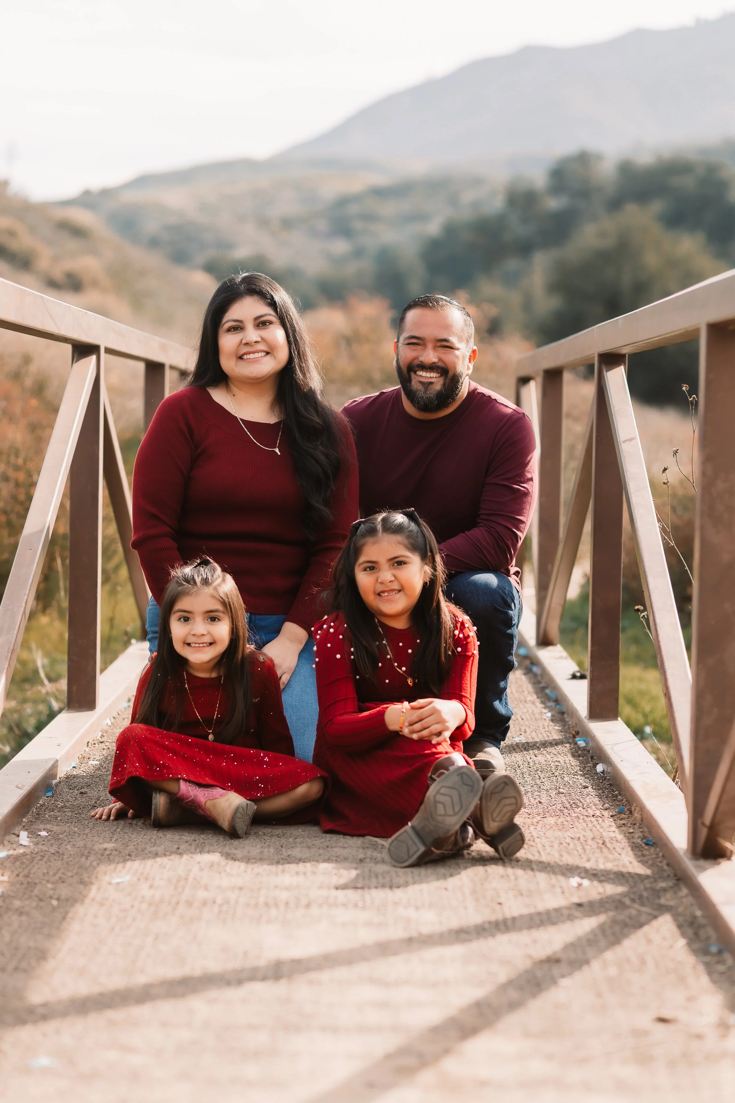 Family of four in matching maroon outfits smiling on a bridge, Santa Clarita