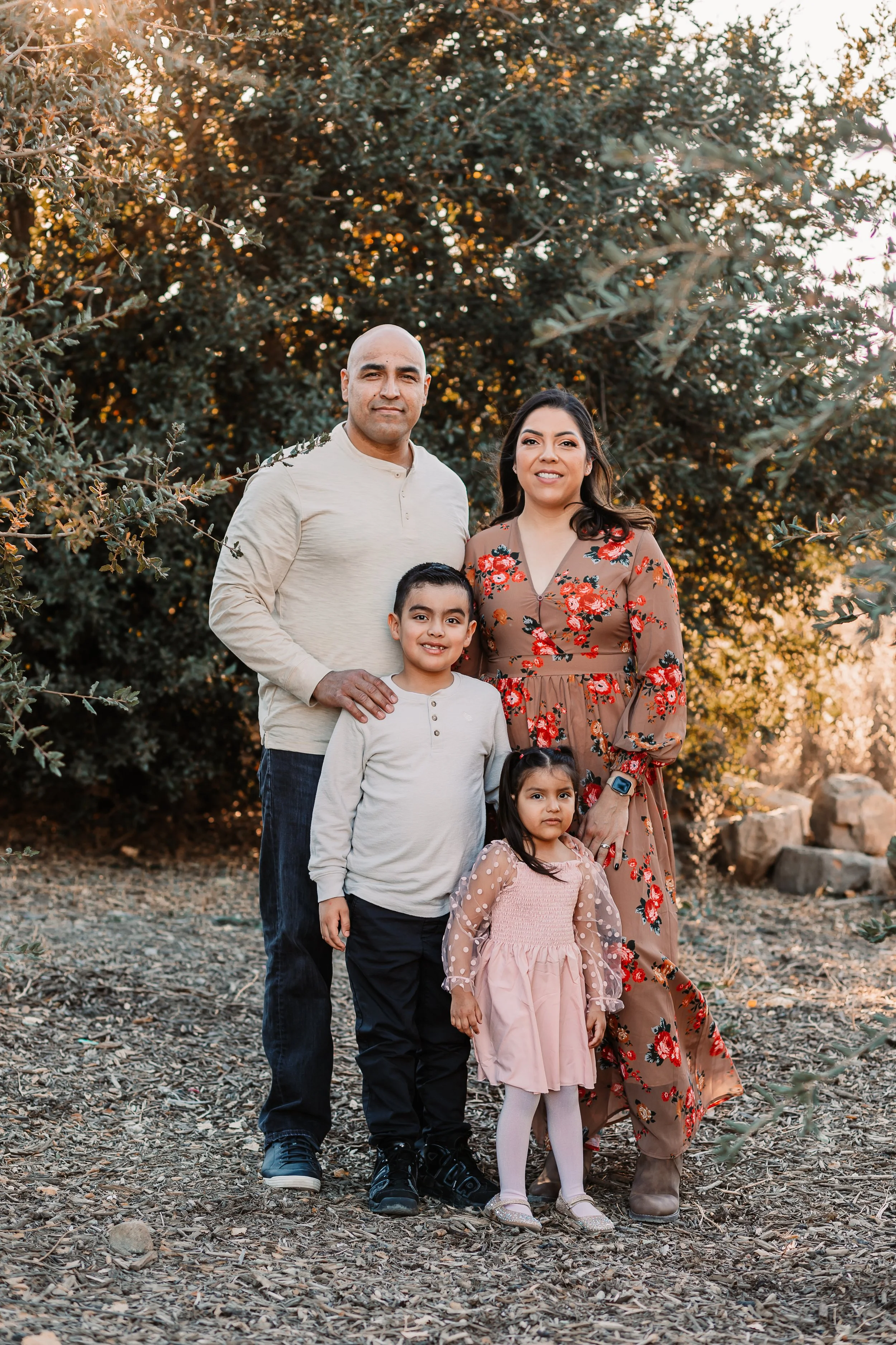 Family of four smiling together on a trail among golden California hills at sunset