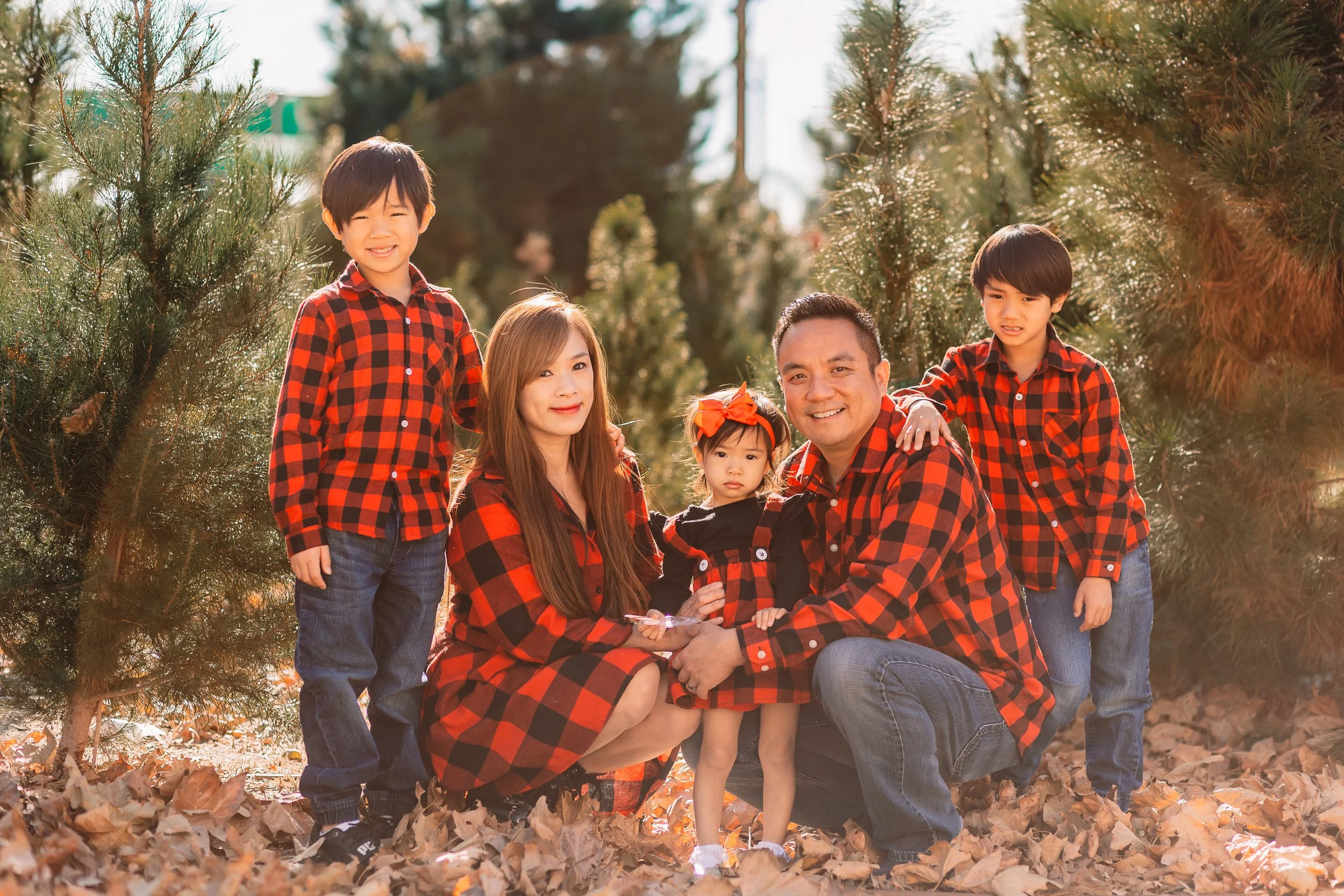 Family of five in matching red and black buffalo plaid among the Christmas trees at a Santa Clarita tree farm.