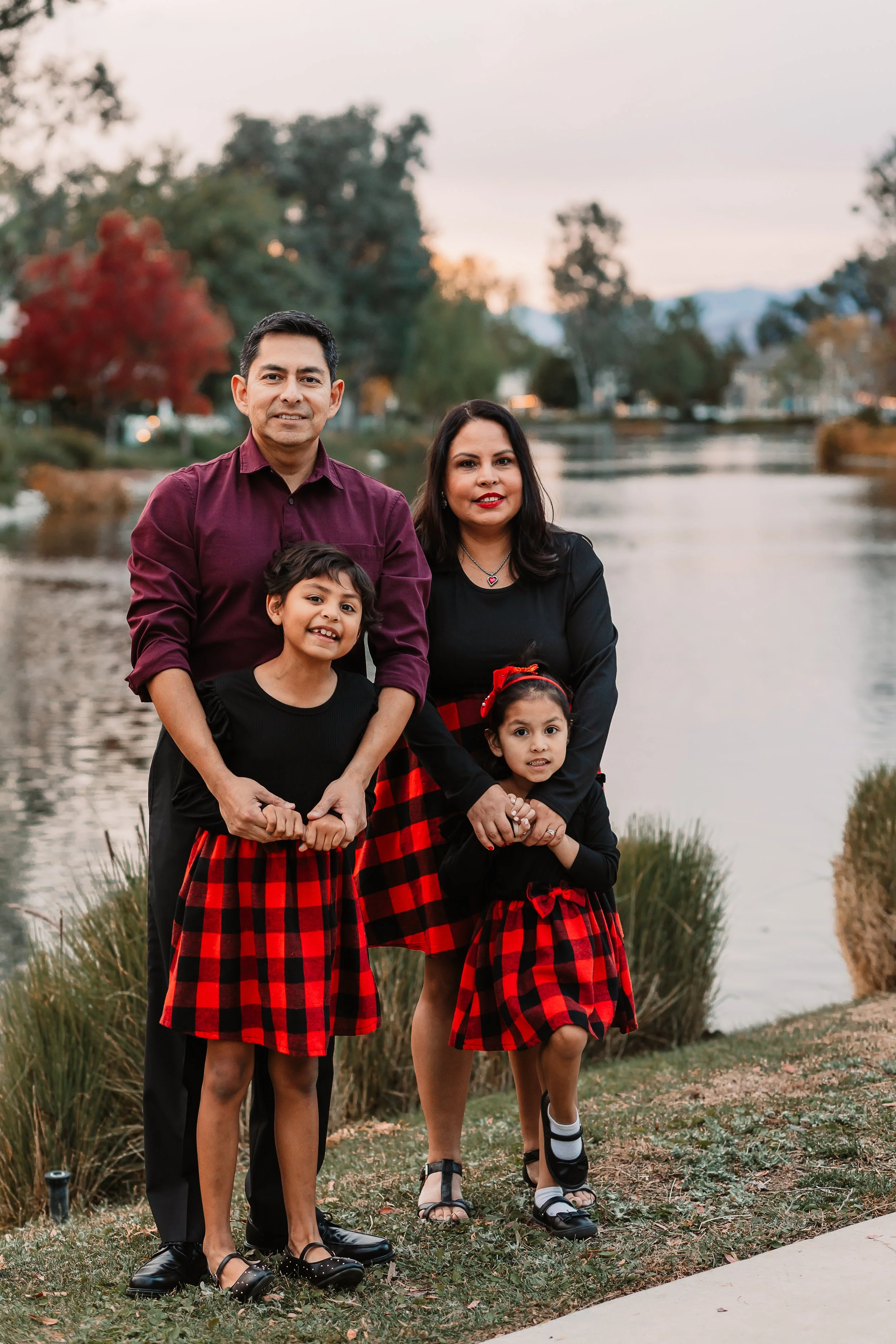 Family of four smiling together by the lake in holiday red plaid outfits