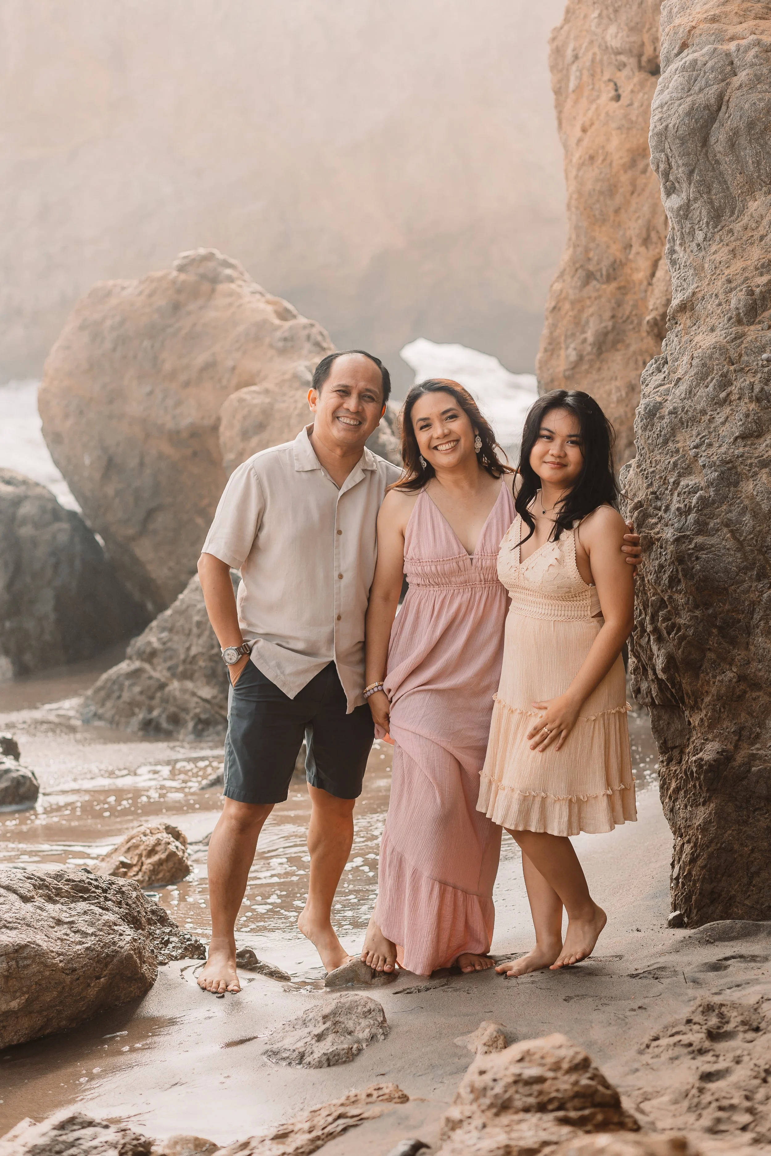 Family of three smiling together between beach rocks at sunset in Santa Clarita