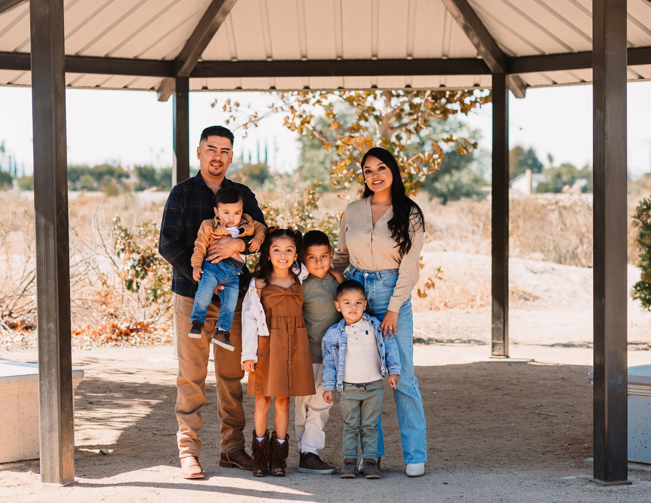 Family of seven smiling together under a park gazebo in warm sunlight