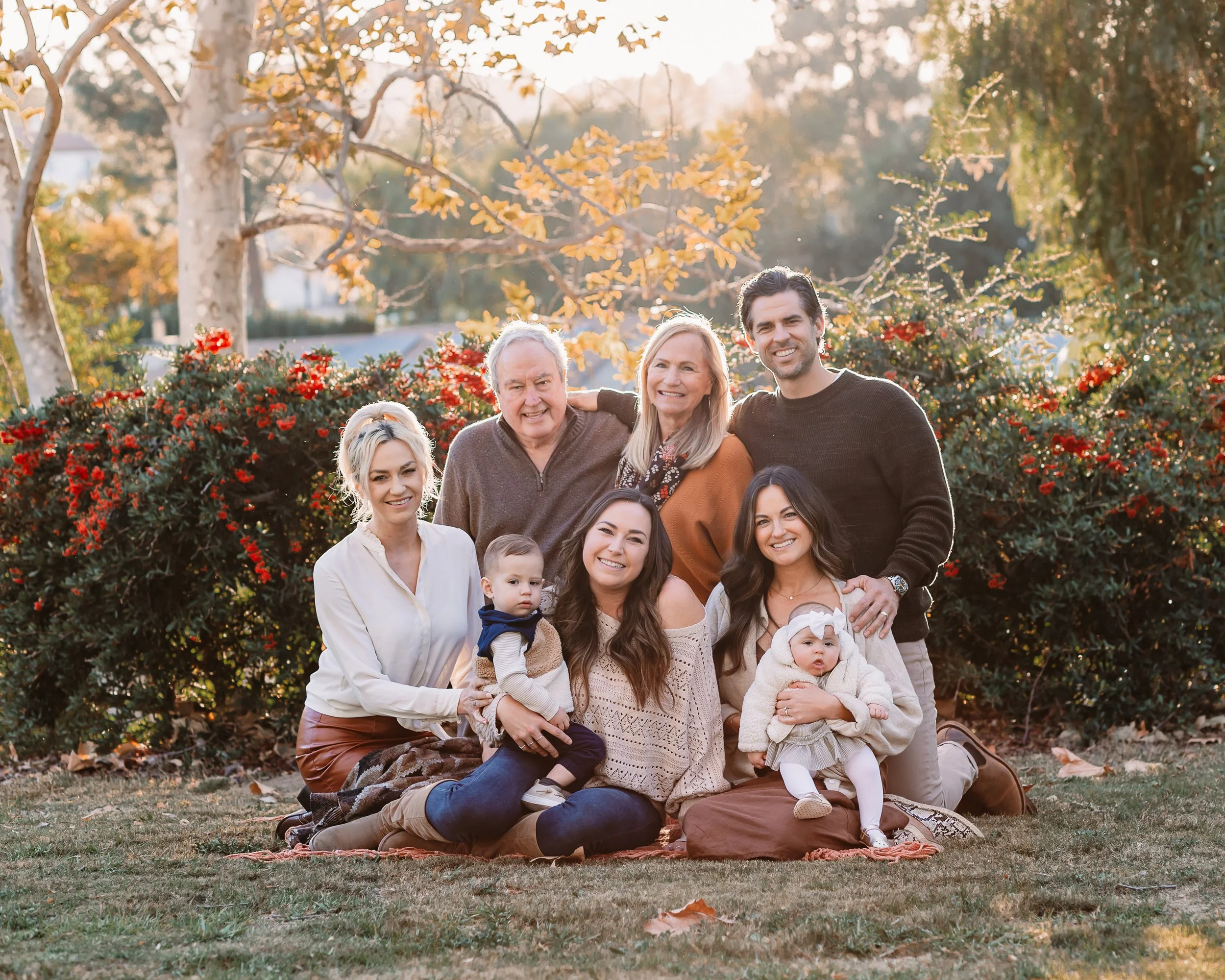 Large extended family smiling together in a sunny park at golden hour