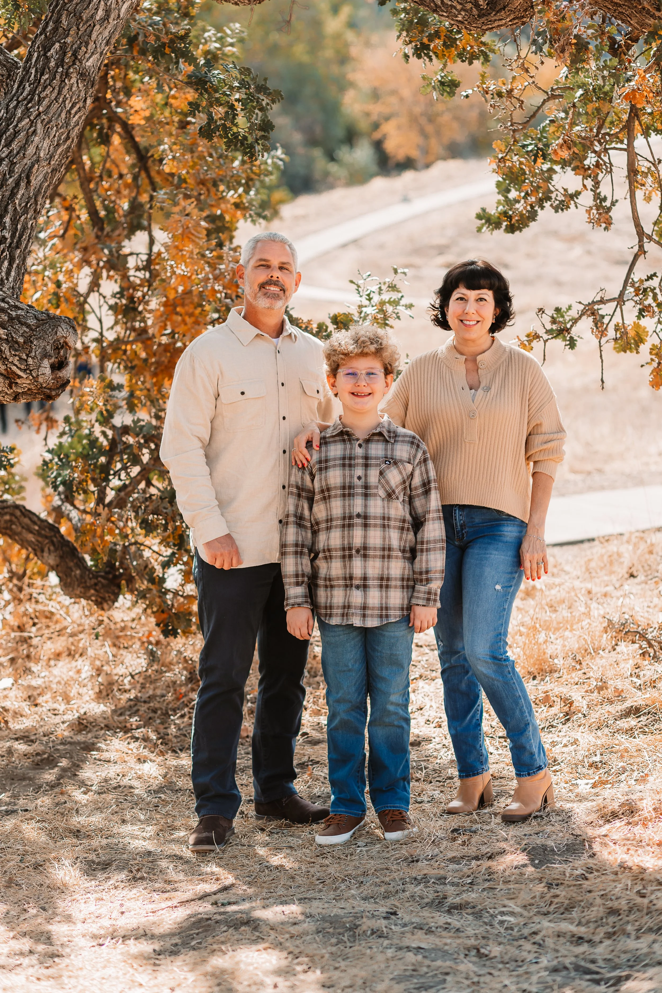 Family of three smiling under oak tree branches in a Santa Clarita park