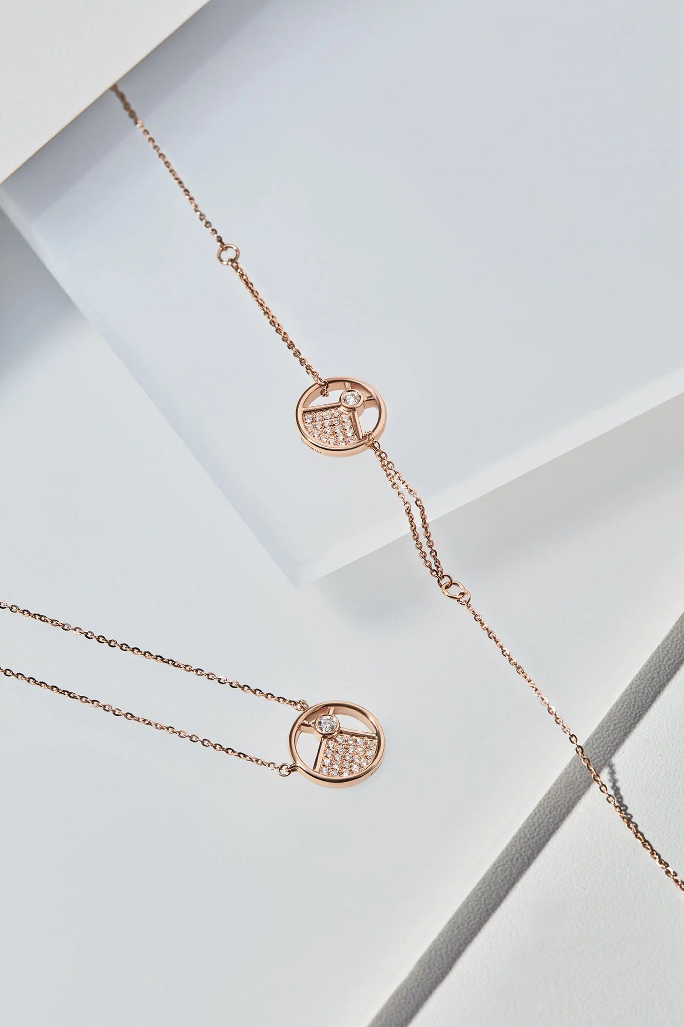 A pair of rose gold bracelets with circular pendants featuring a small diamond and pave-set diamonds, placed on a white surface.
