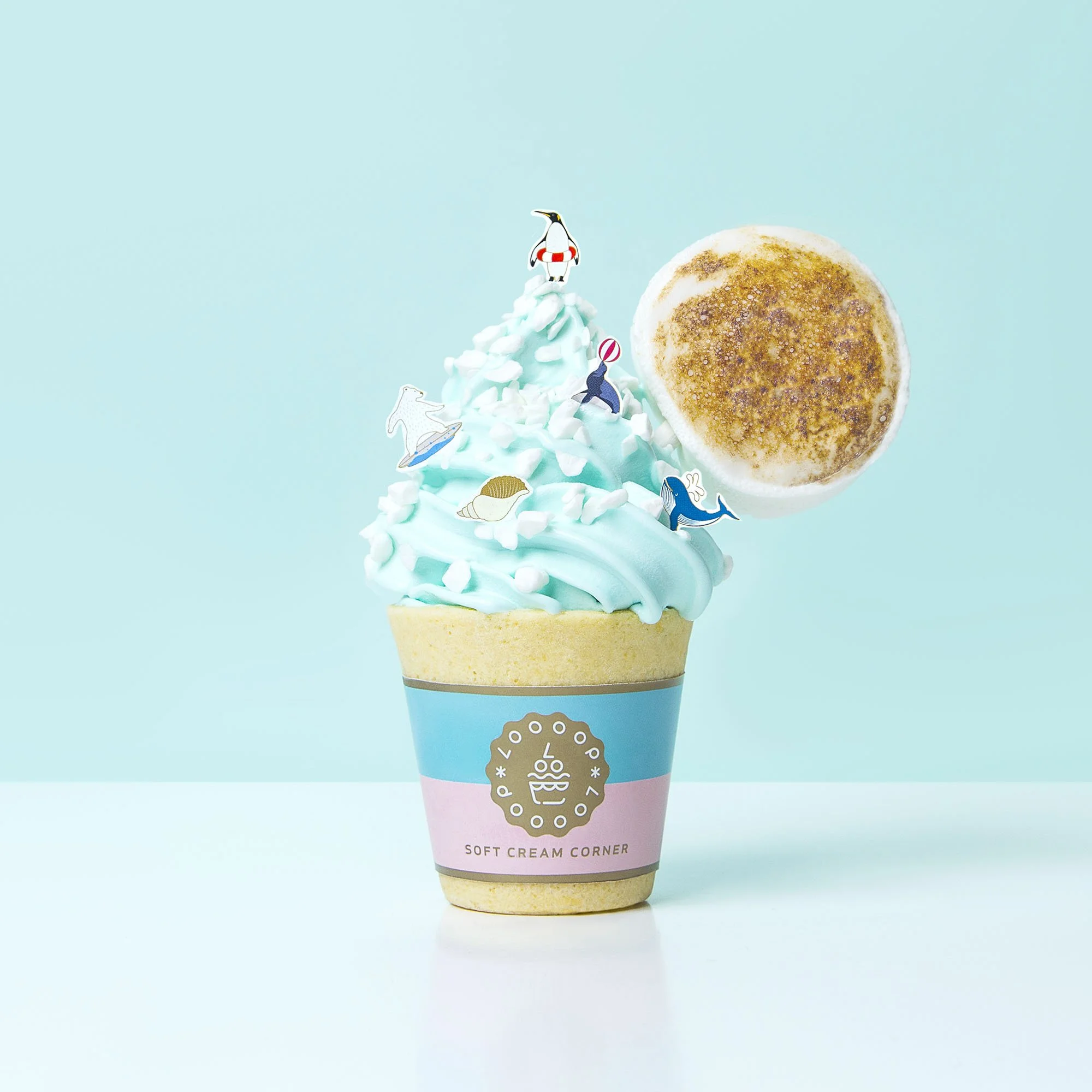 Ice cream cone with blue frosting, sea animal confetti, and a cinnamon sugar donut on a pastel blue background.