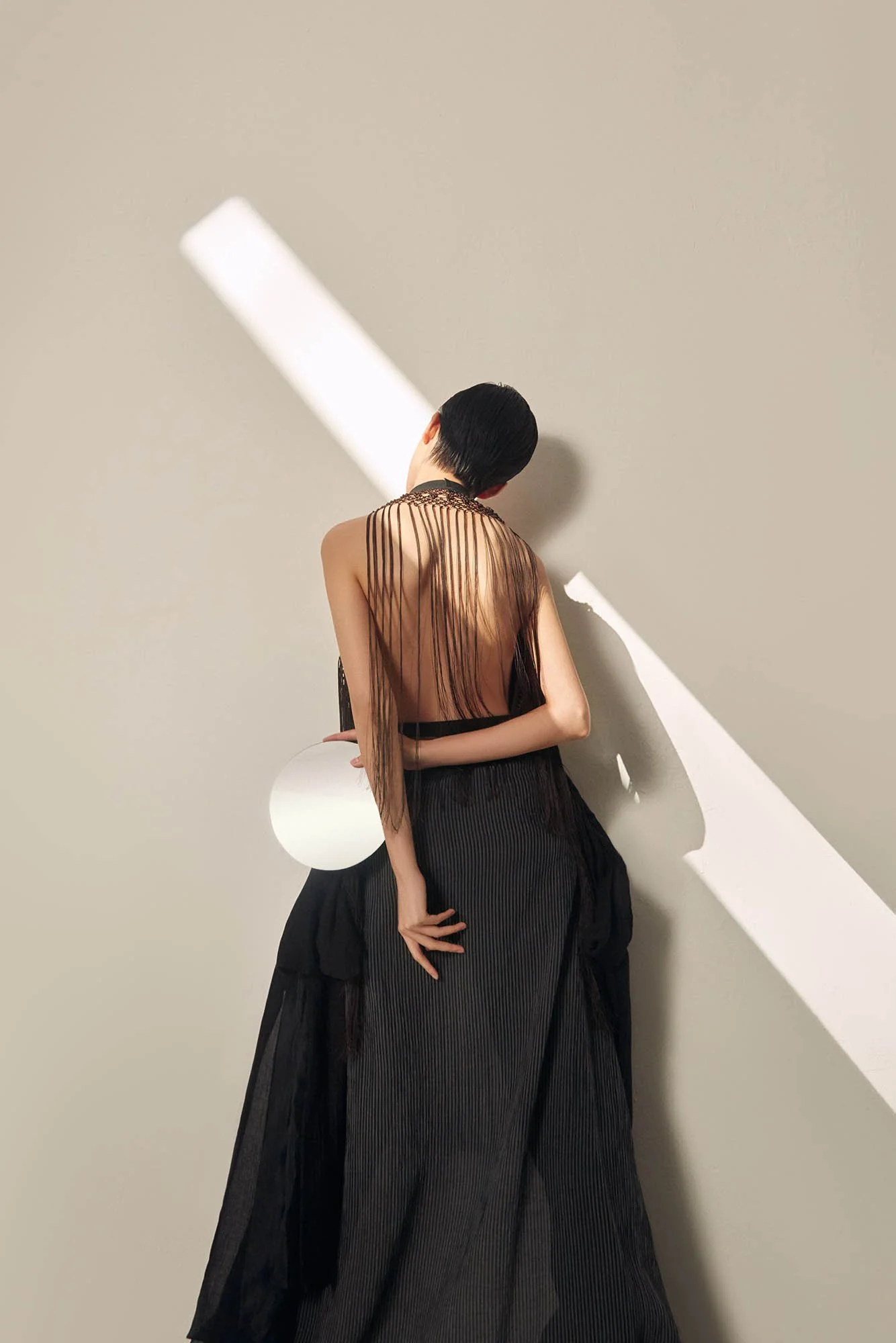 Woman in a sheer black dress standing against a wall with unusual lighting effects.