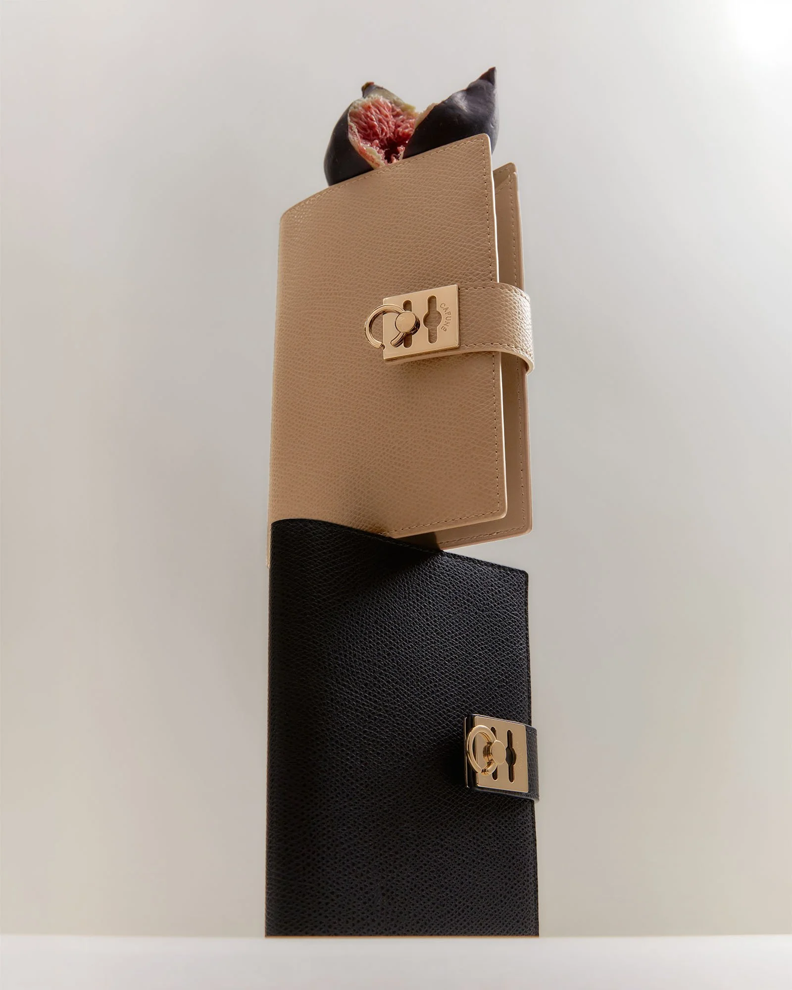 Two black wallets with gold hardware, one beige and one black, stacked vertically and placed on a white surface against a plain background.