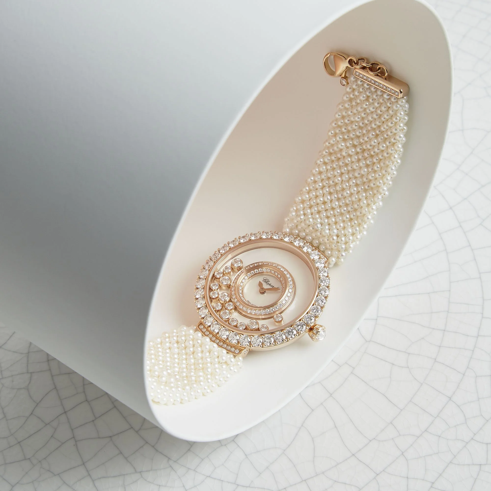 A luxurious wristwatch with a pearl strap and a diamond-studded face, displayed inside a white oval box.