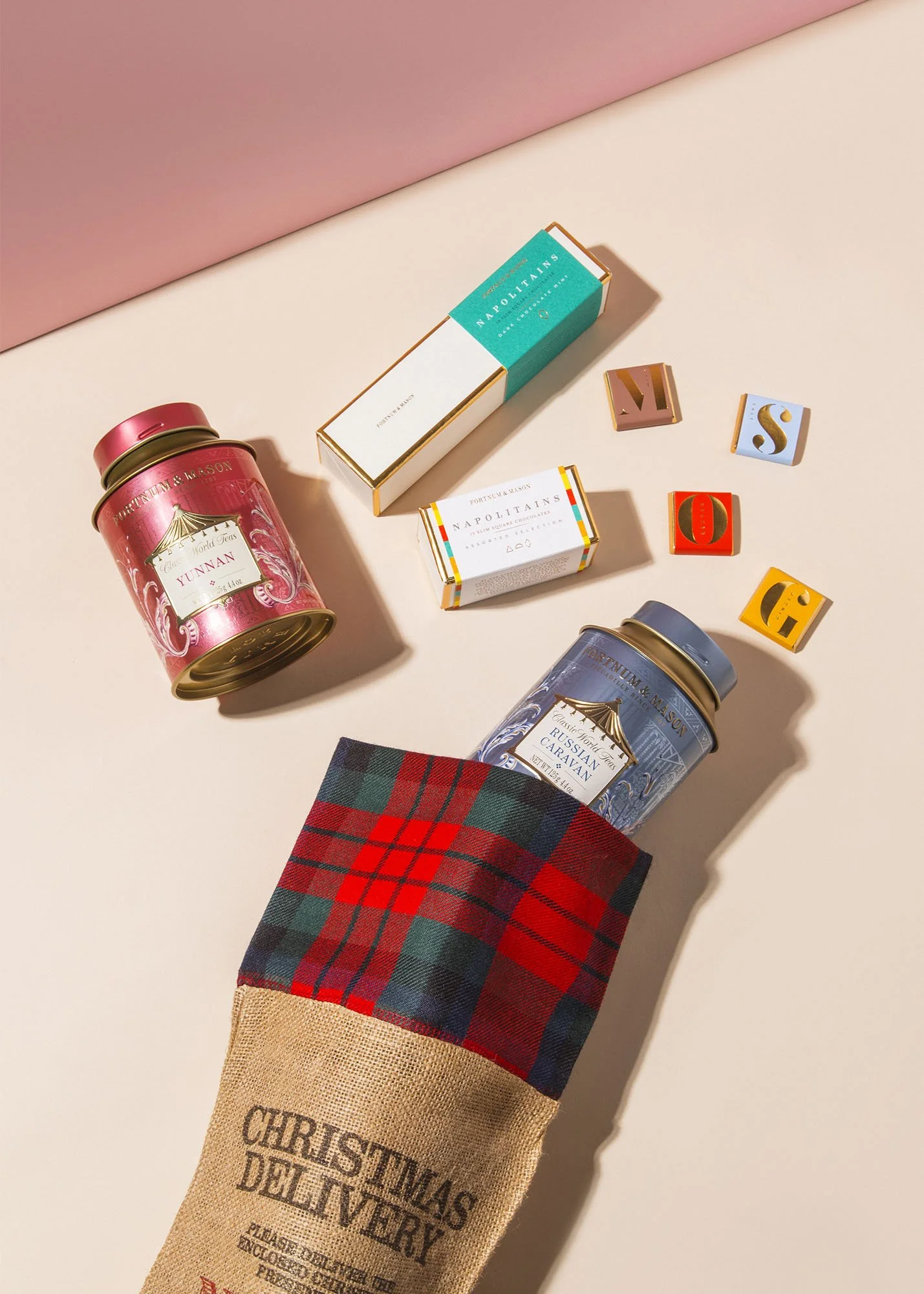 Two tins of chocolates and three small decorative blocks with letters spelling 'S', 'V', and 'O'. A Christmas-themed sack with checked pattern holds one tin.