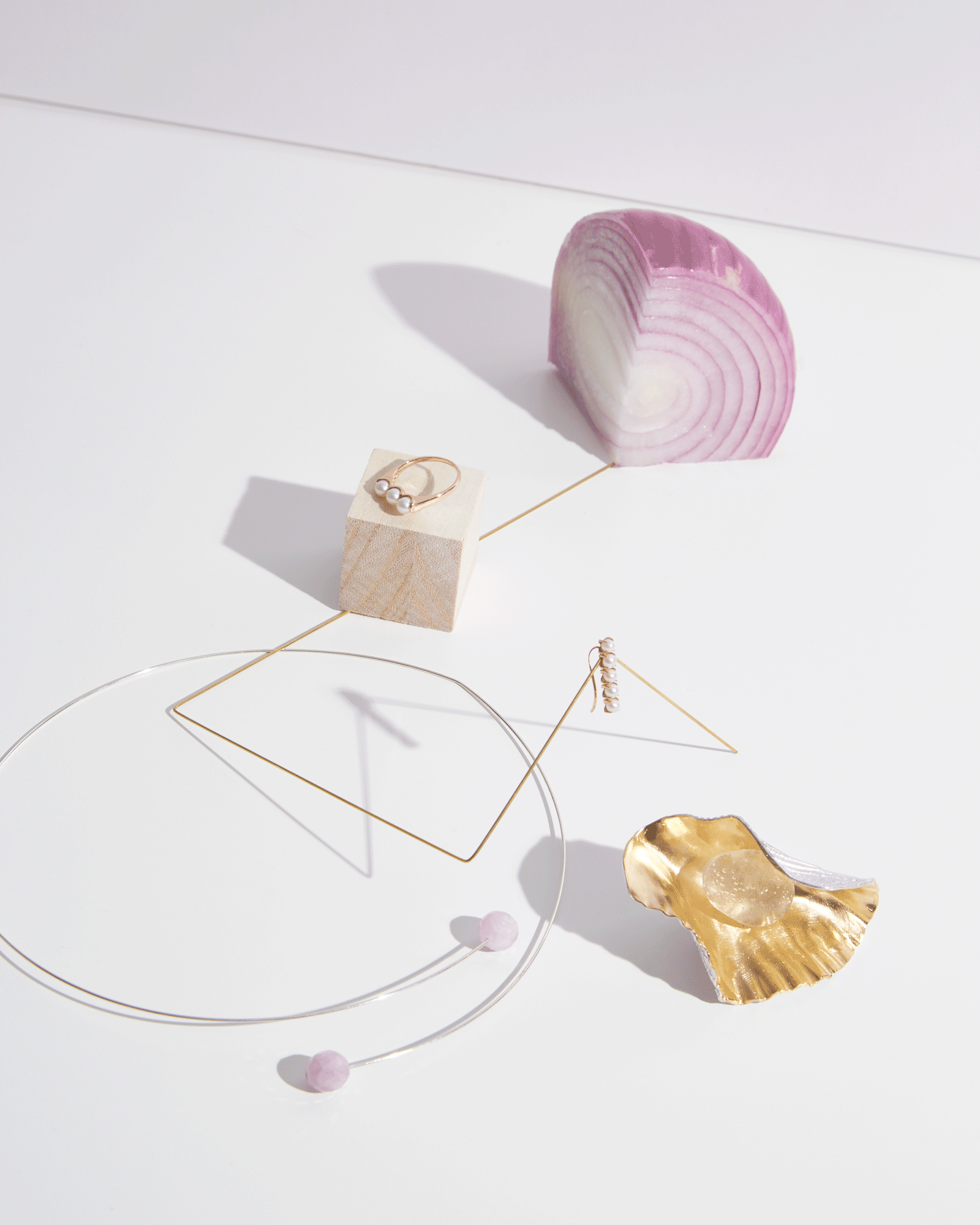 Jewelry display with pearl earrings and ring, decorative wire shapes, a purple onion, and a gold seashell on a white surface.