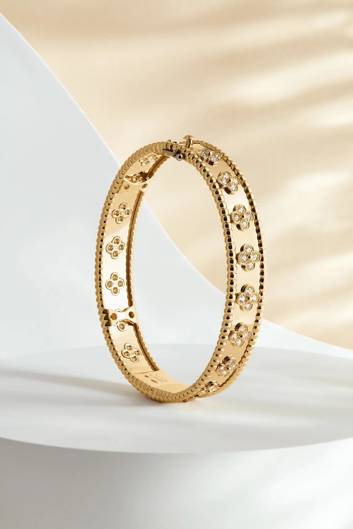 Gold bracelet with floral design encased with small diamonds, displayed on a white and beige background.