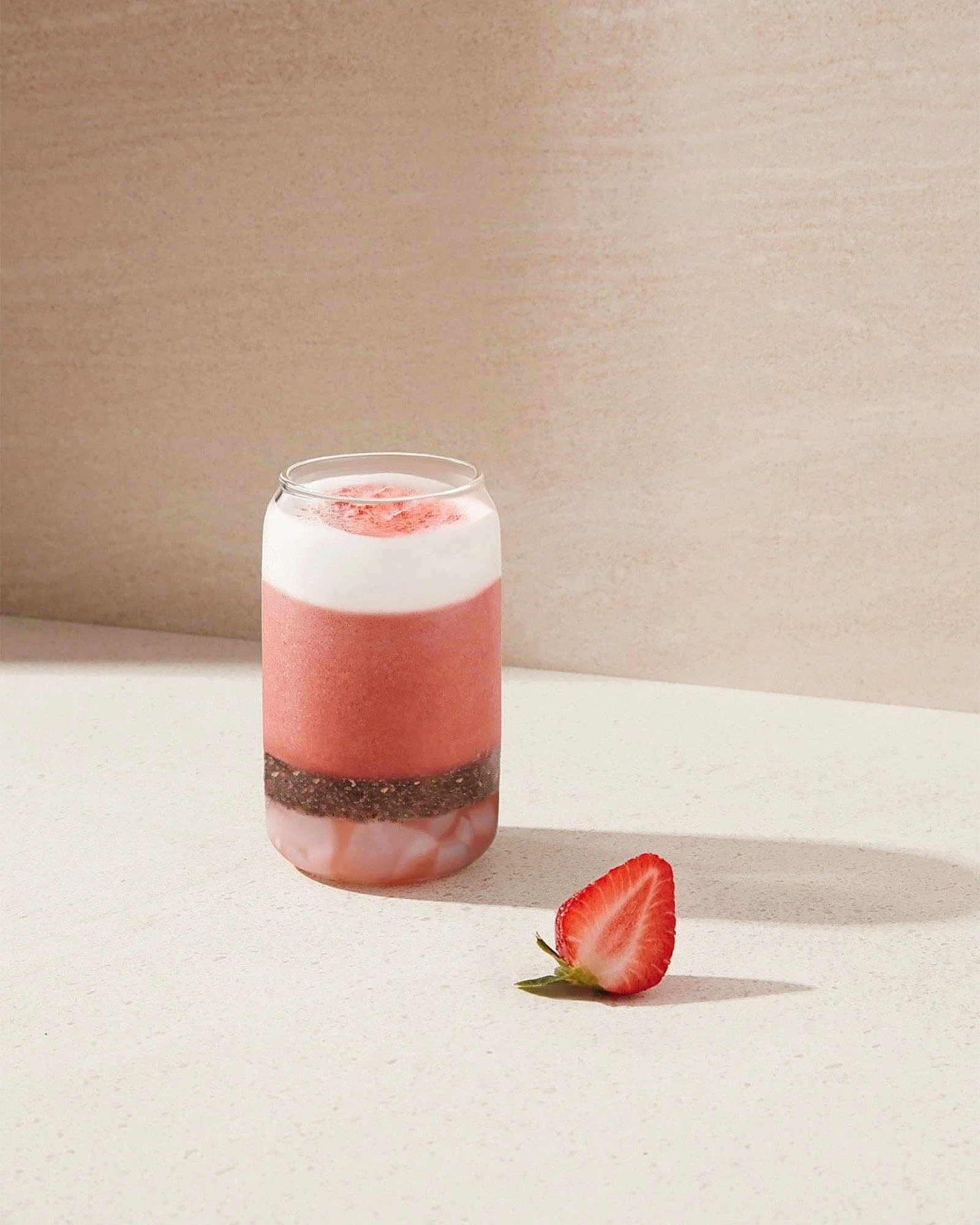 A layered pink and white dessert in a jar with a strawberry half on the table beside it.