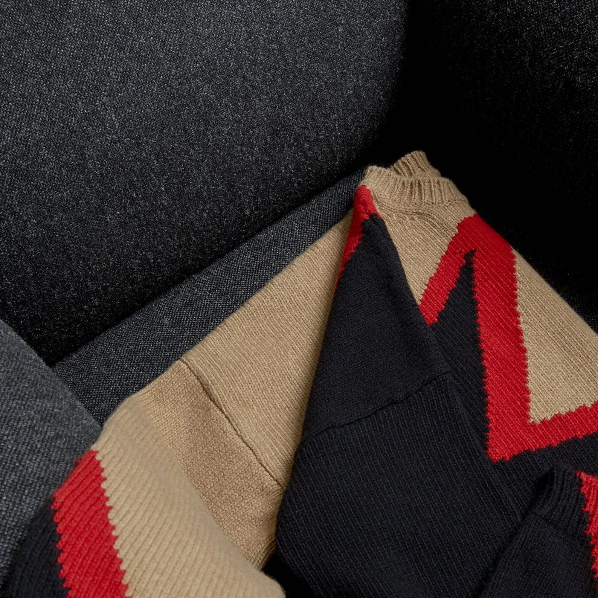 Close-up of a folded sweater with red and black design against a black background.