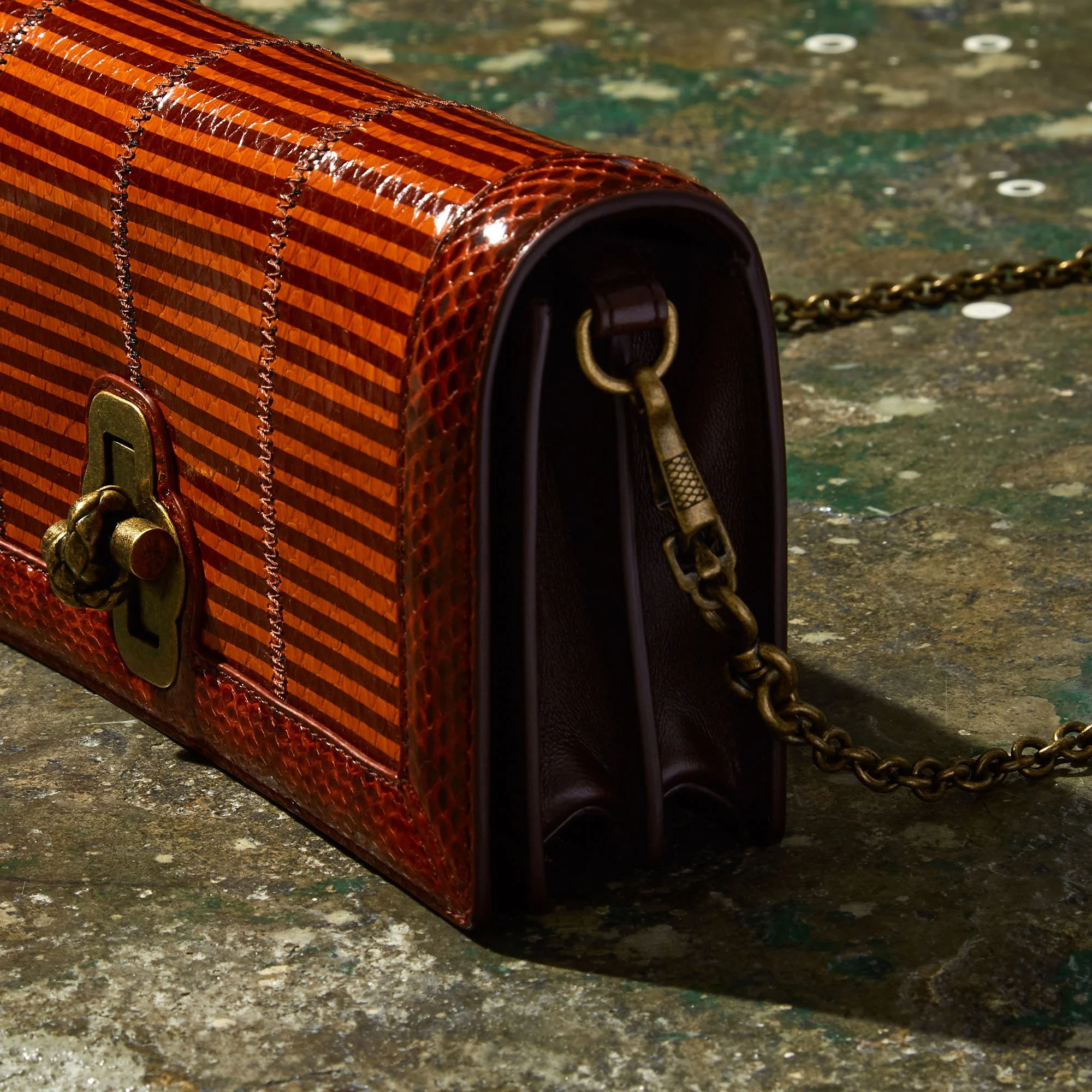 A vintage handbag with a chain strap on a textured surface.