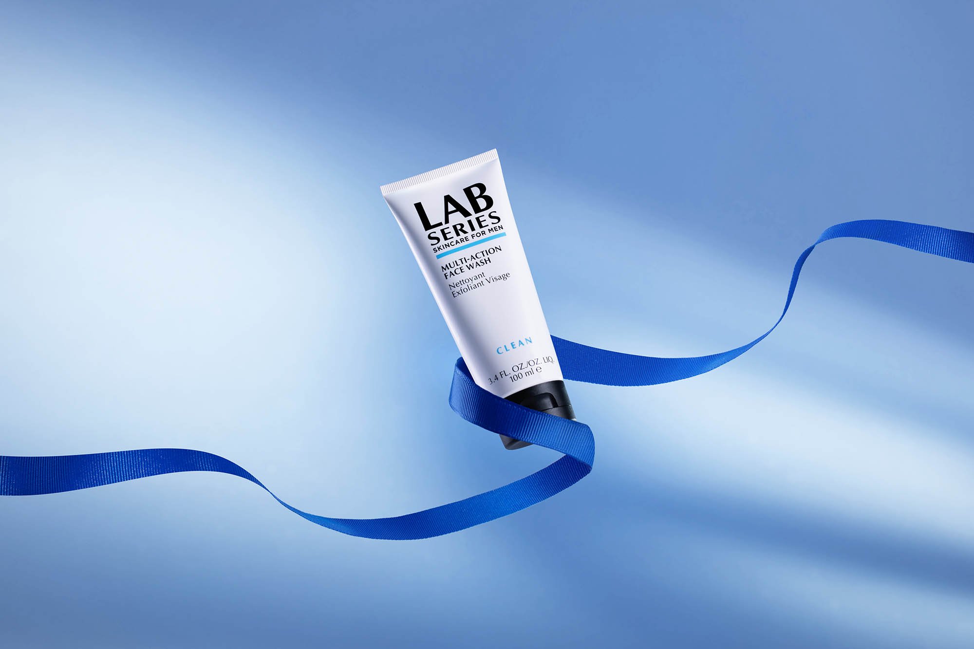 A tube of Lab Series Multi-Action Face Wash floating over a light blue background with a blue ribbon curling around it.