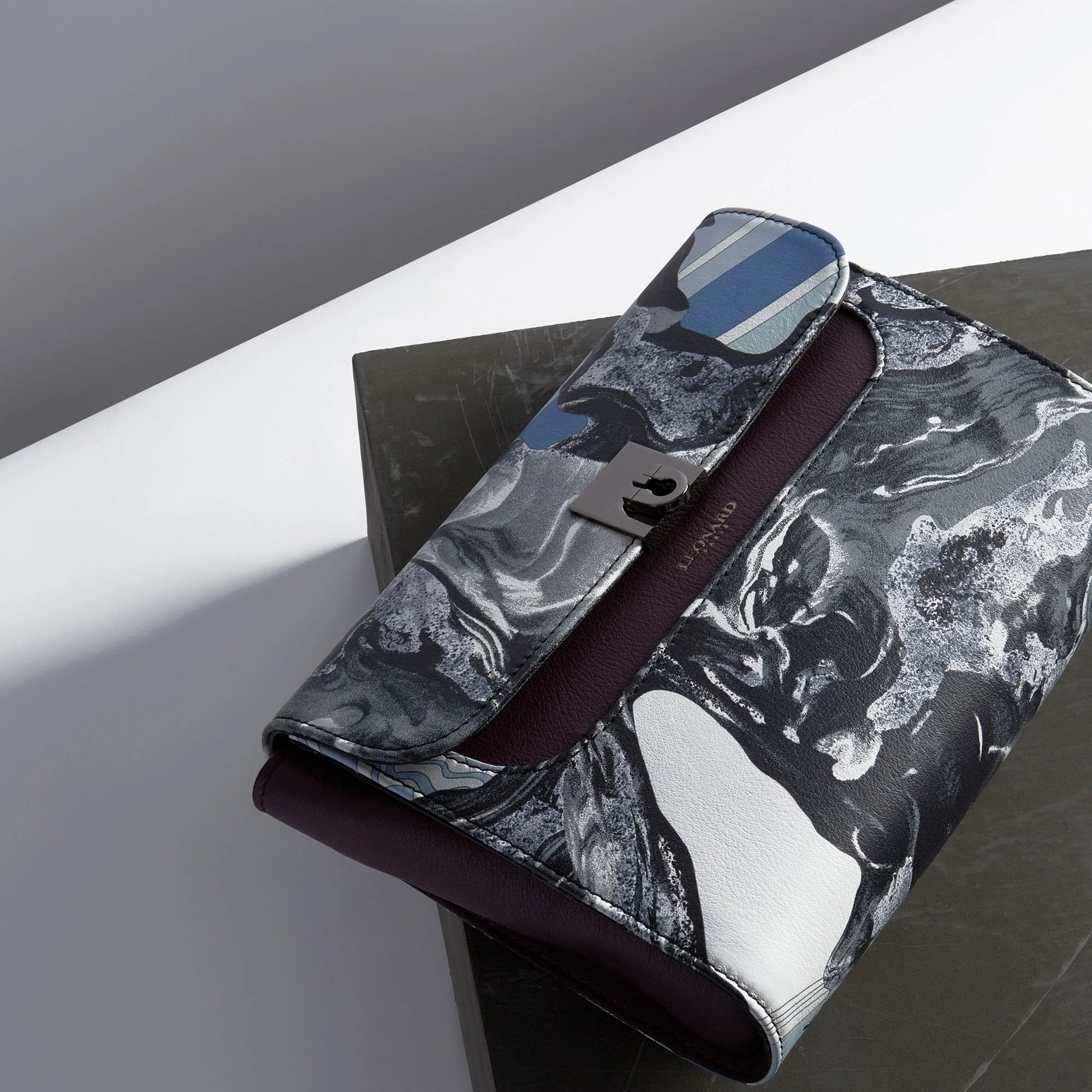 Fashion clutch bag with a marbled black, white, and blue design, placed on a dark and white surface.