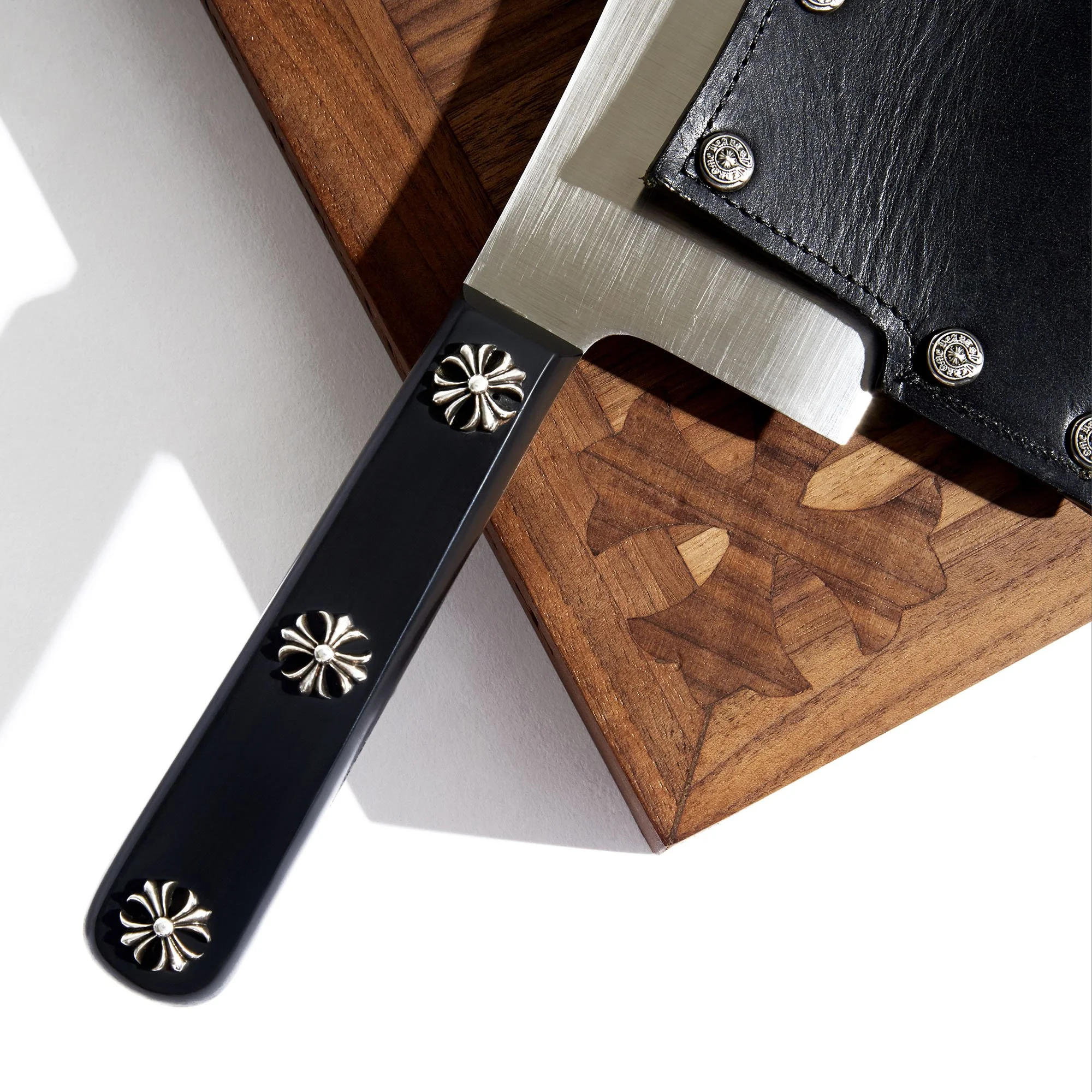 Close-up of a black leather item with silver studs, resting on a metal surface on a wooden background.