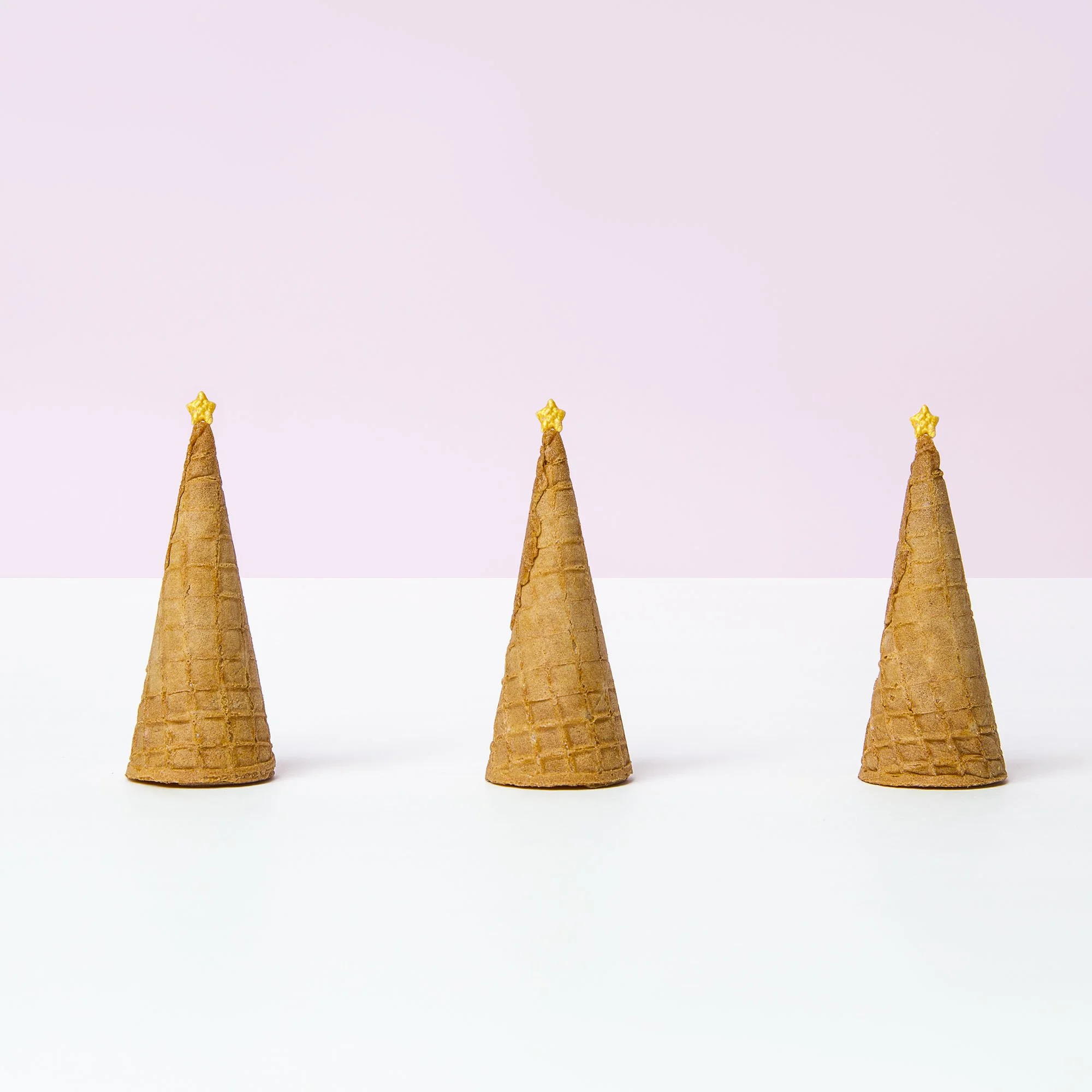Three ice cream cones decorated as Christmas trees with star toppers, arranged in a row against a minimalist background.
