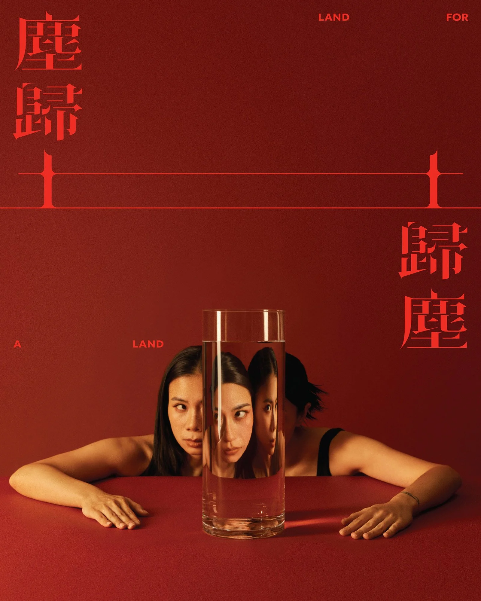 Two women with dark hair laying on a red surface, with a tall glass of water between them. Their faces are reflected in the glass, creating a threefold mirror effect. Red text in Japanese characters and the phrase 'LAND FOR' is on the red background.