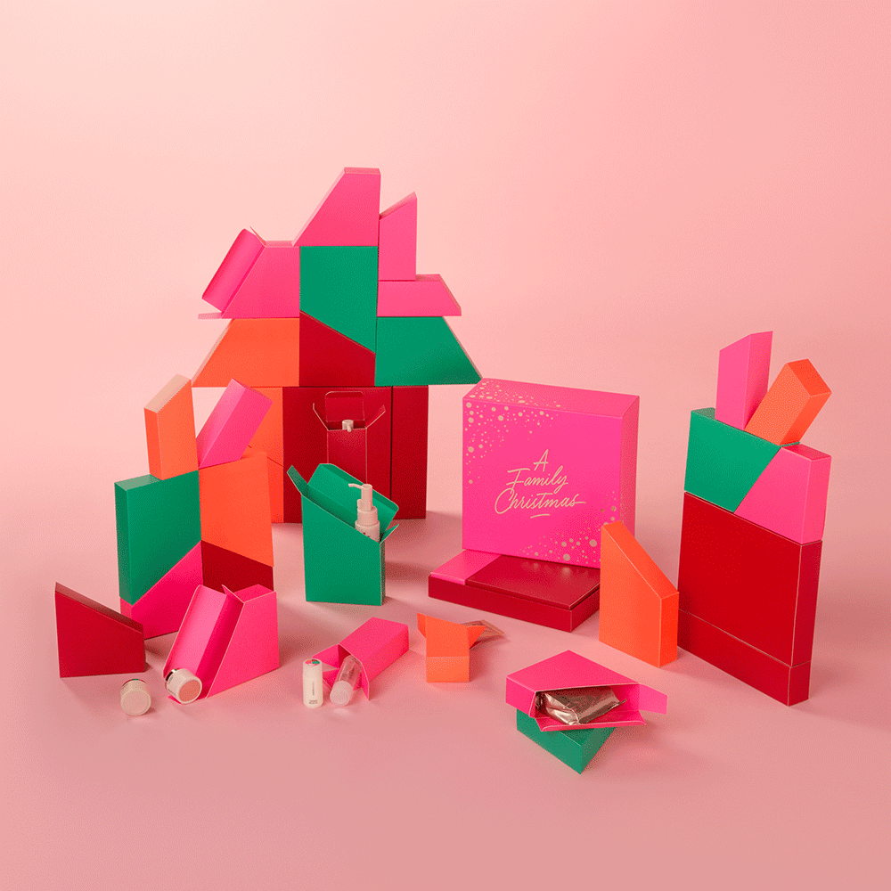 Colorful Christmas gift boxes and packaging materials in pink, red, green, and orange with a pink box labeled "A Family Christmas" on a pink background.