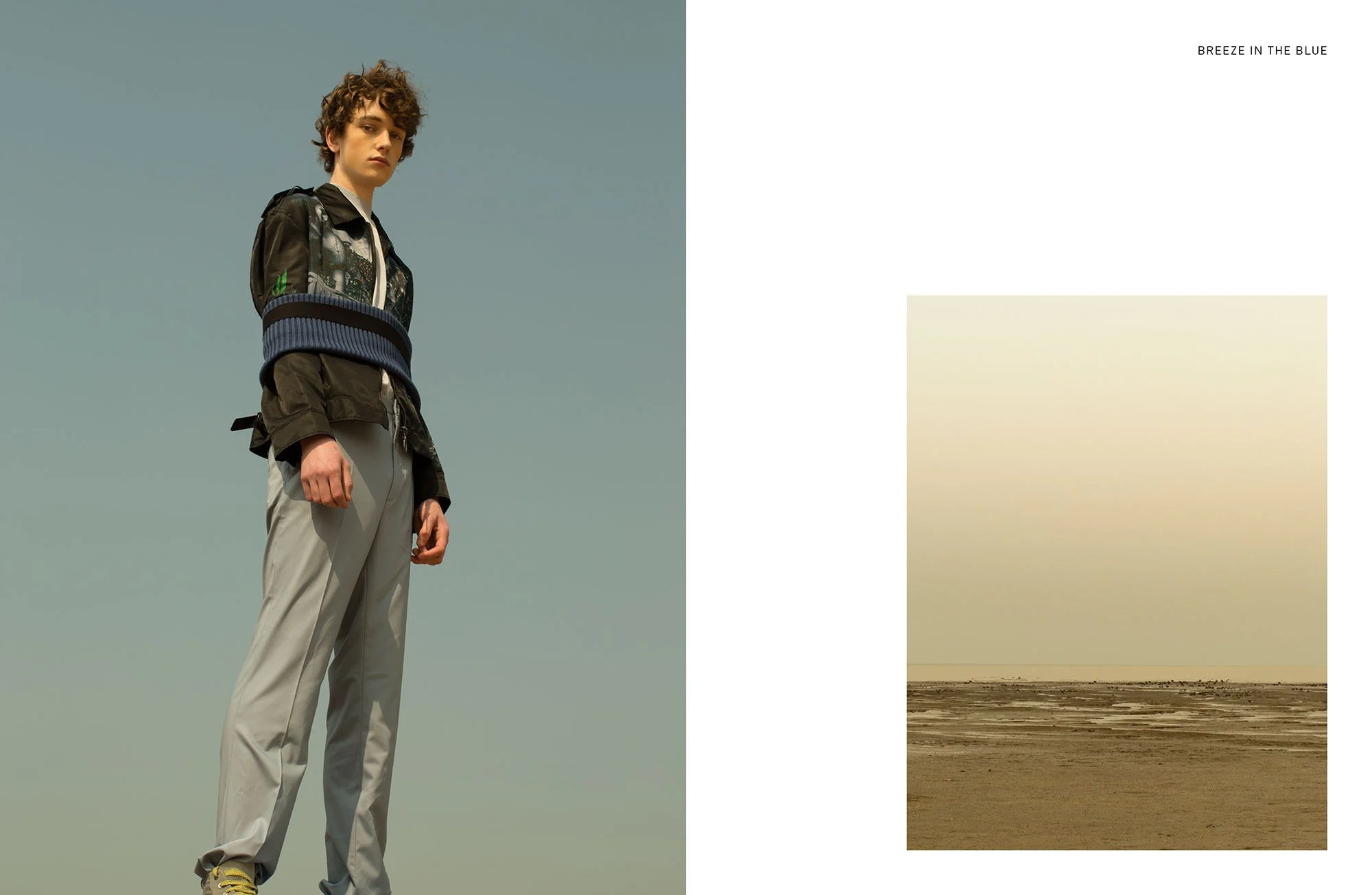 A fashion photo split into two sections: on the left, a young person with short curly hair wearing a dark jacket and light-colored pants, standing against a clear sky; on the right, a minimalistic landscape with a cloudy sky above a dry, cracked land