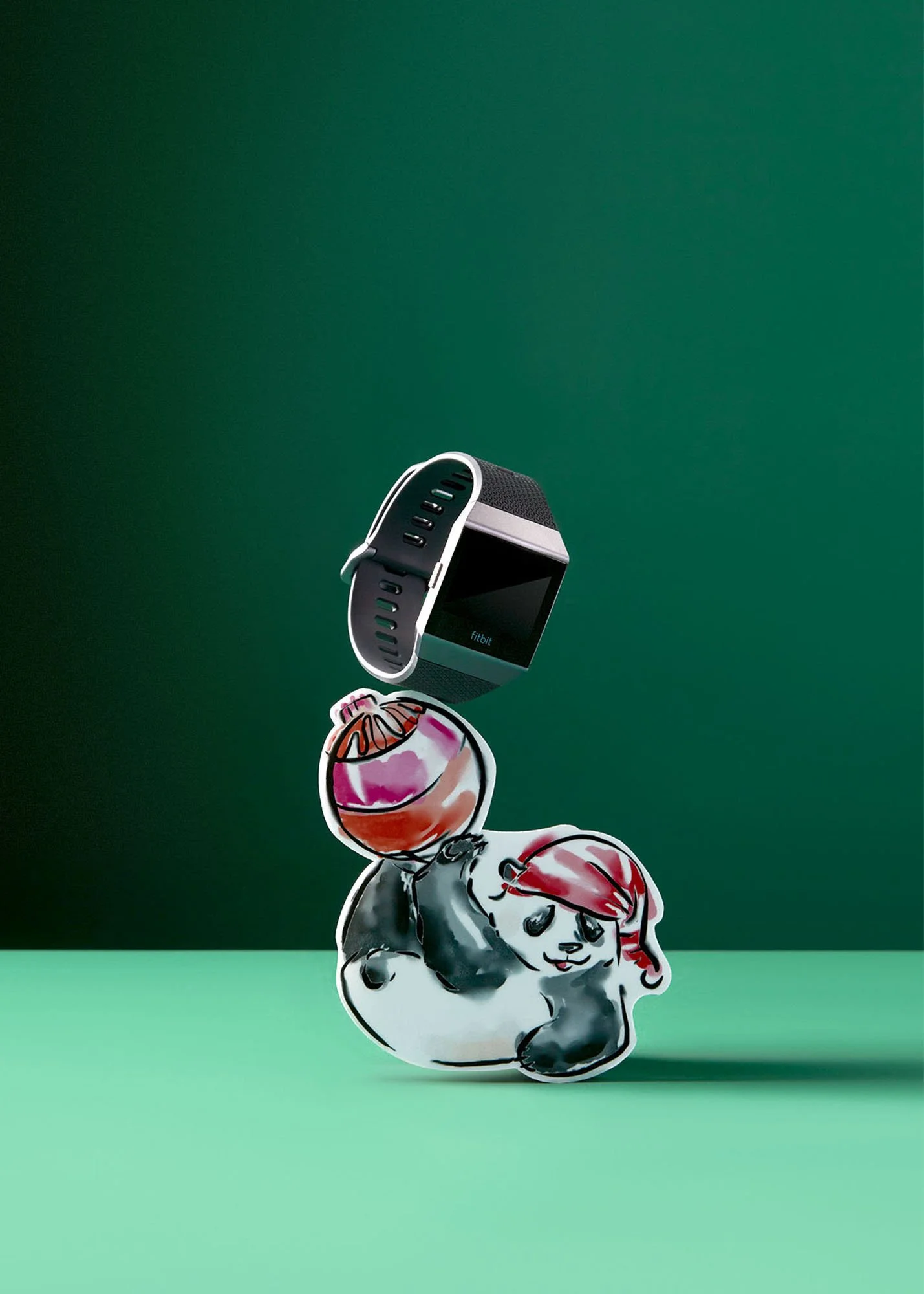 A cartoon black and white dog with red hair lying on a green surface, with a Fitbit smartwatch floating above it and a pink and peach ornament between them, against a dark green background.