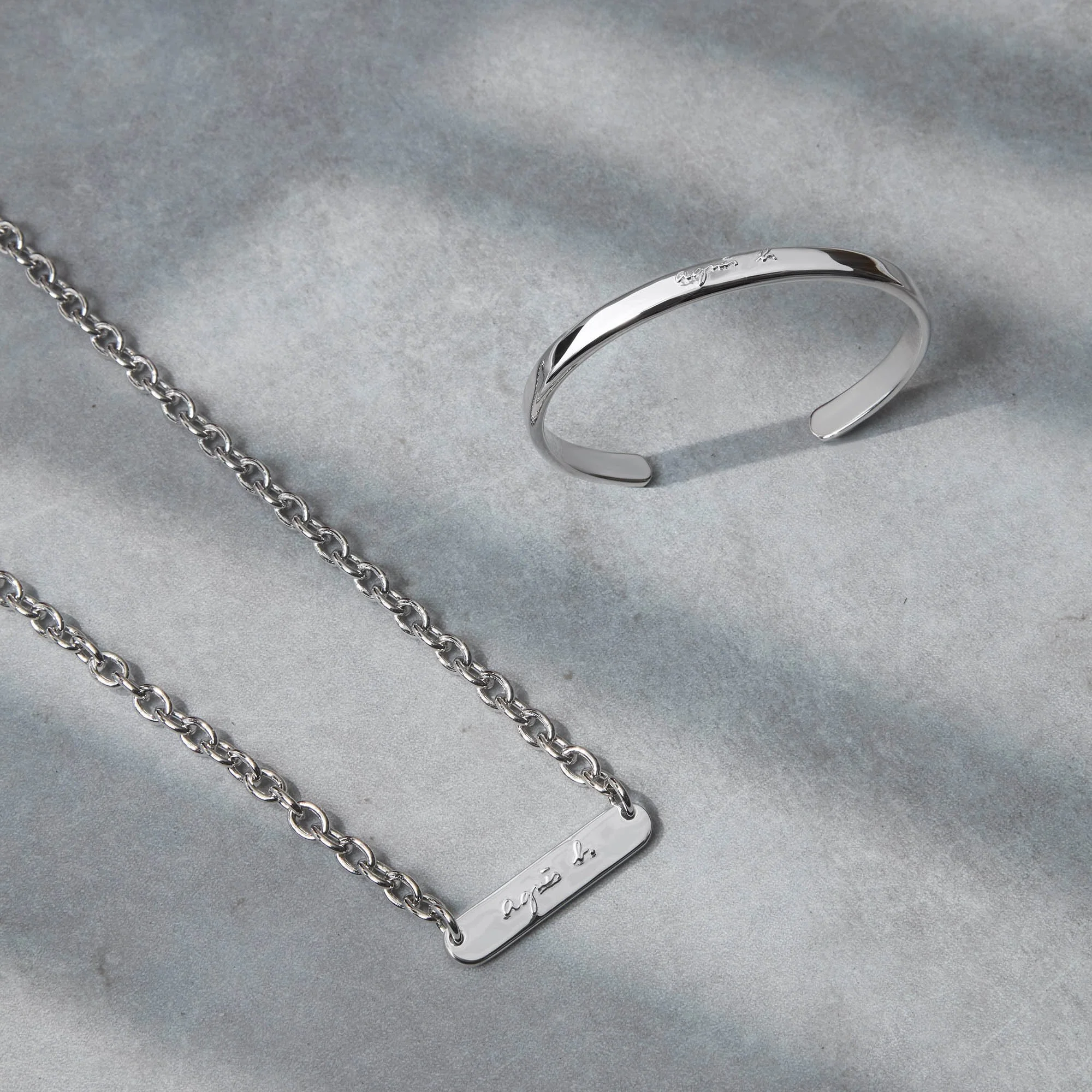 Silver necklace and bracelet with engraved names on a textured gray surface.